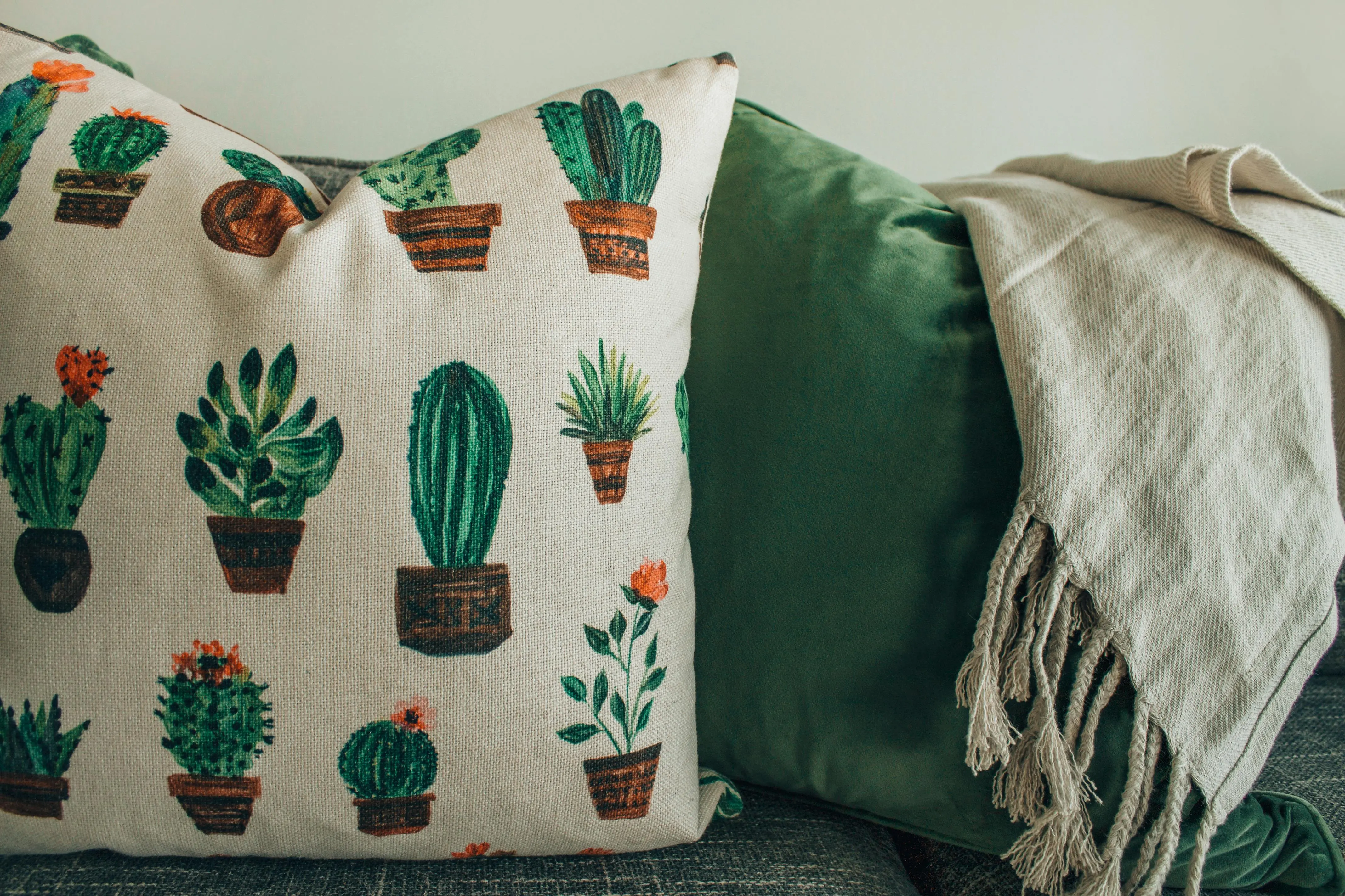 navy throw pillows A cozy modern interior featuring cactus print throw pillows and a soft blanket on a sofa.