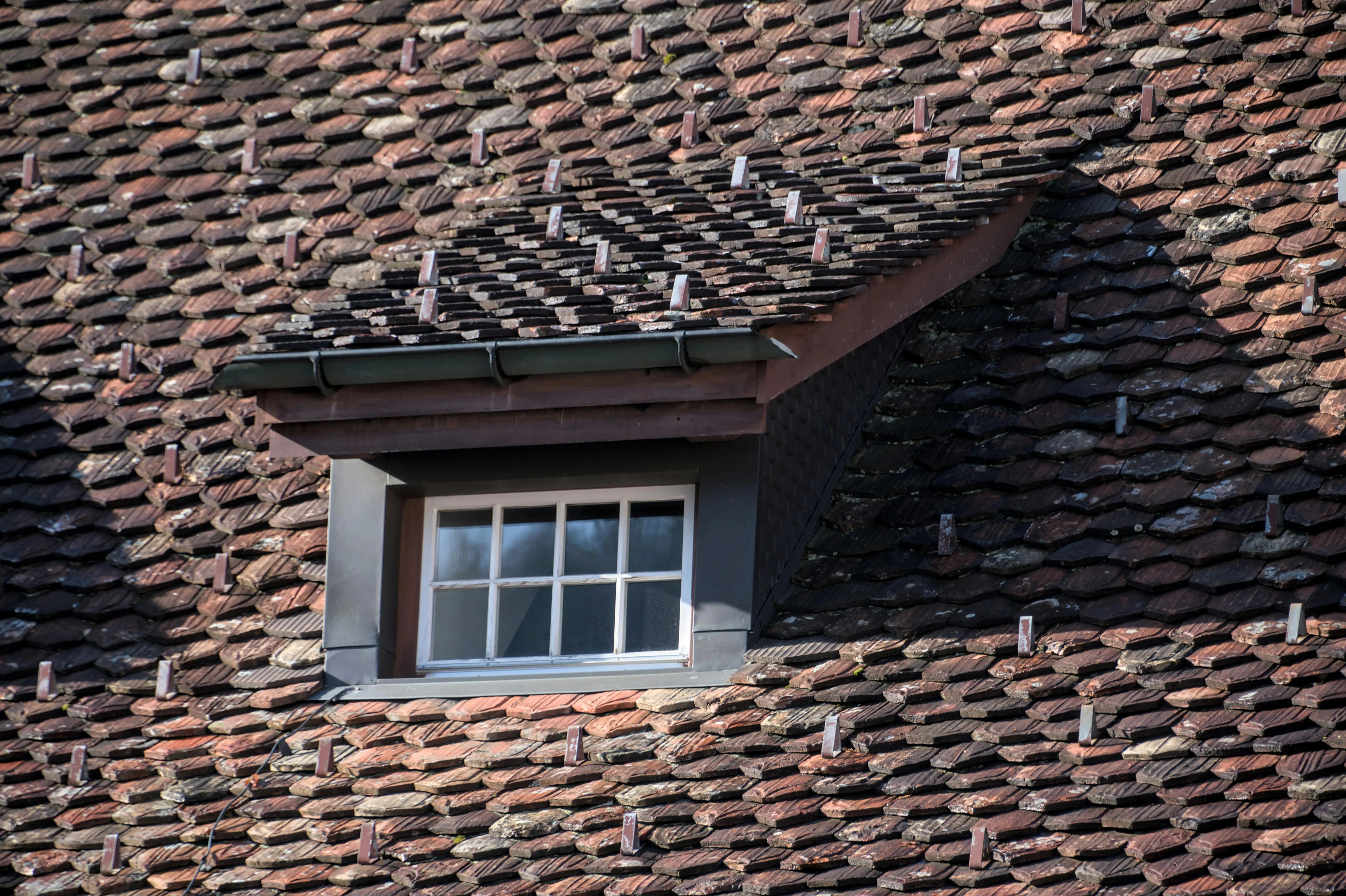 parts of a house exterior Close-up of a vintage rooftop with a dormer window, showcasing unique tile arrangement and architectural details.