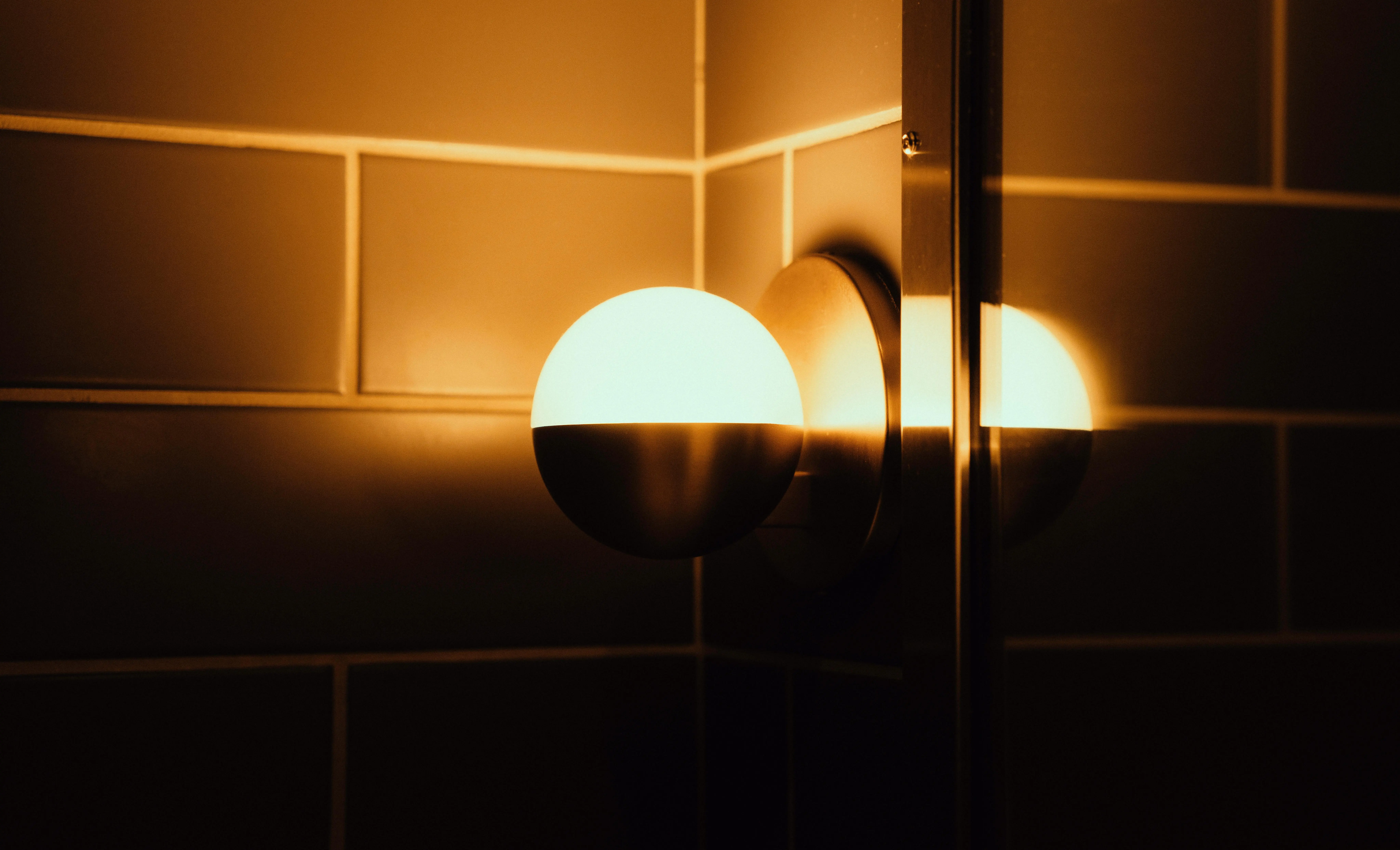 exterior wall sconce lights A close-up of a wall lamp casting a warm glow and reflection on tiled walls.