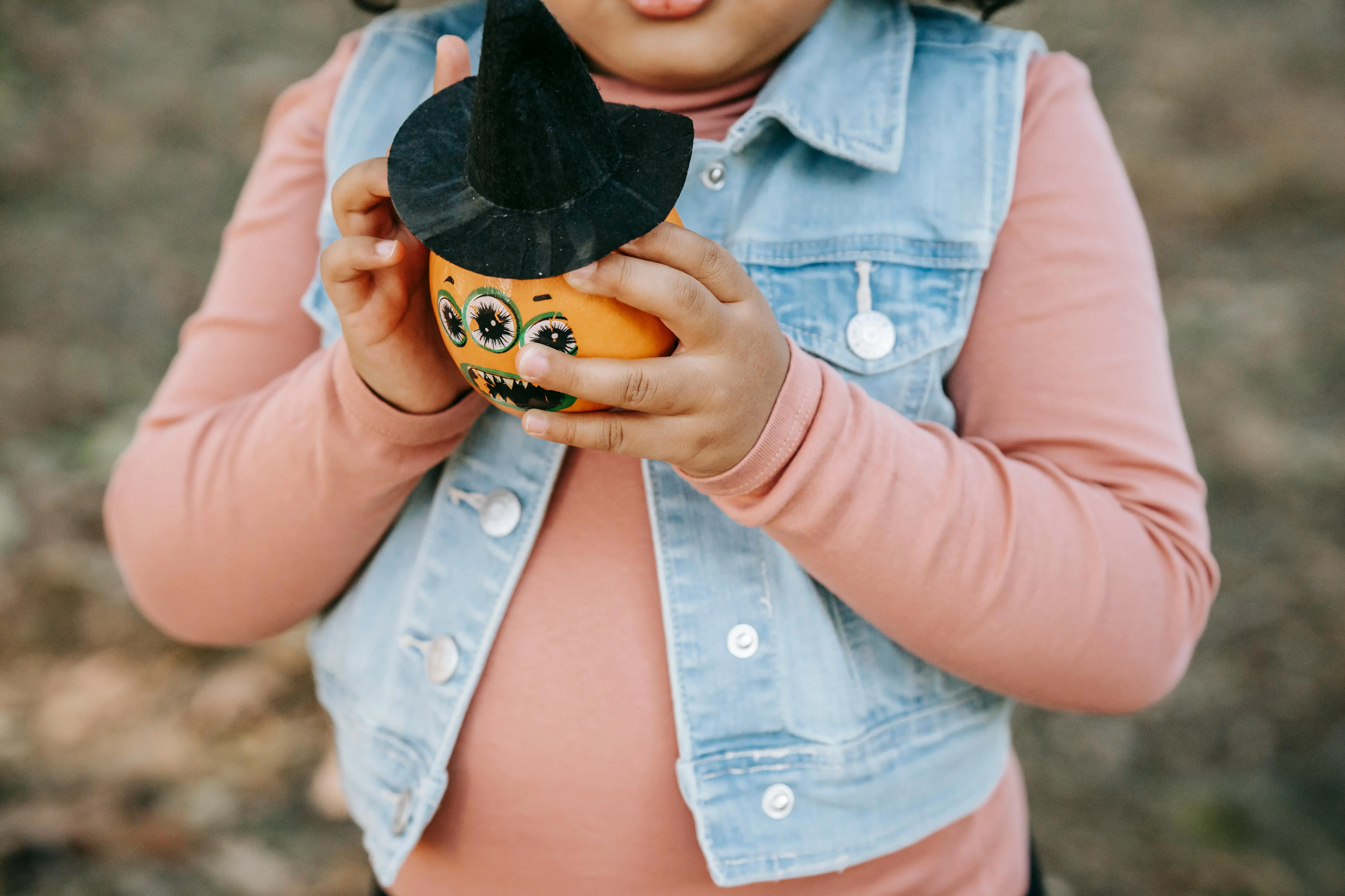cute pumpkin painting ideas Child holding a small decorated pumpkin with a witch hat, perfect for Halloween festivities.