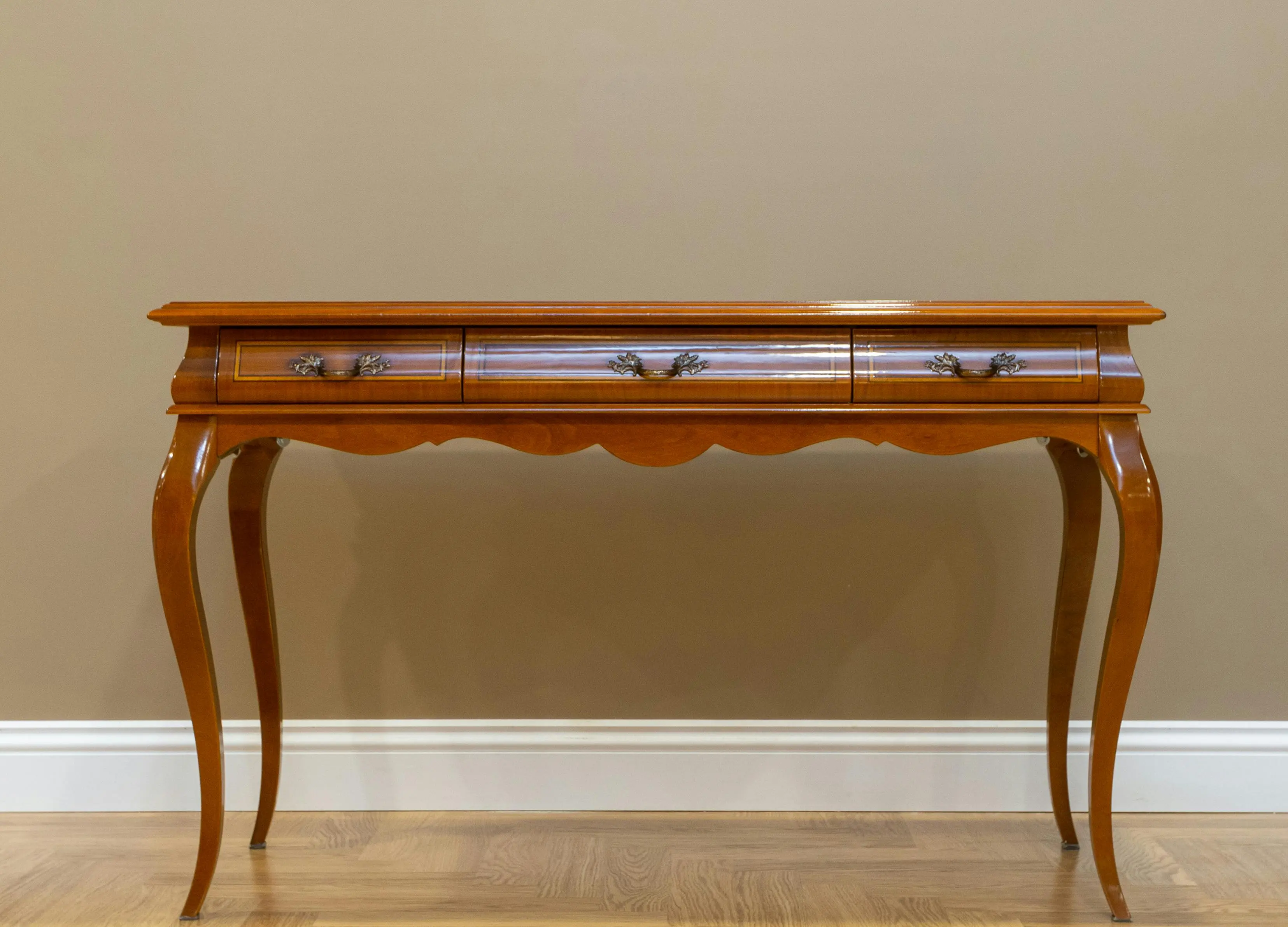 extendable console table Classic wooden console table with elegant design and metal handles against a beige wall.