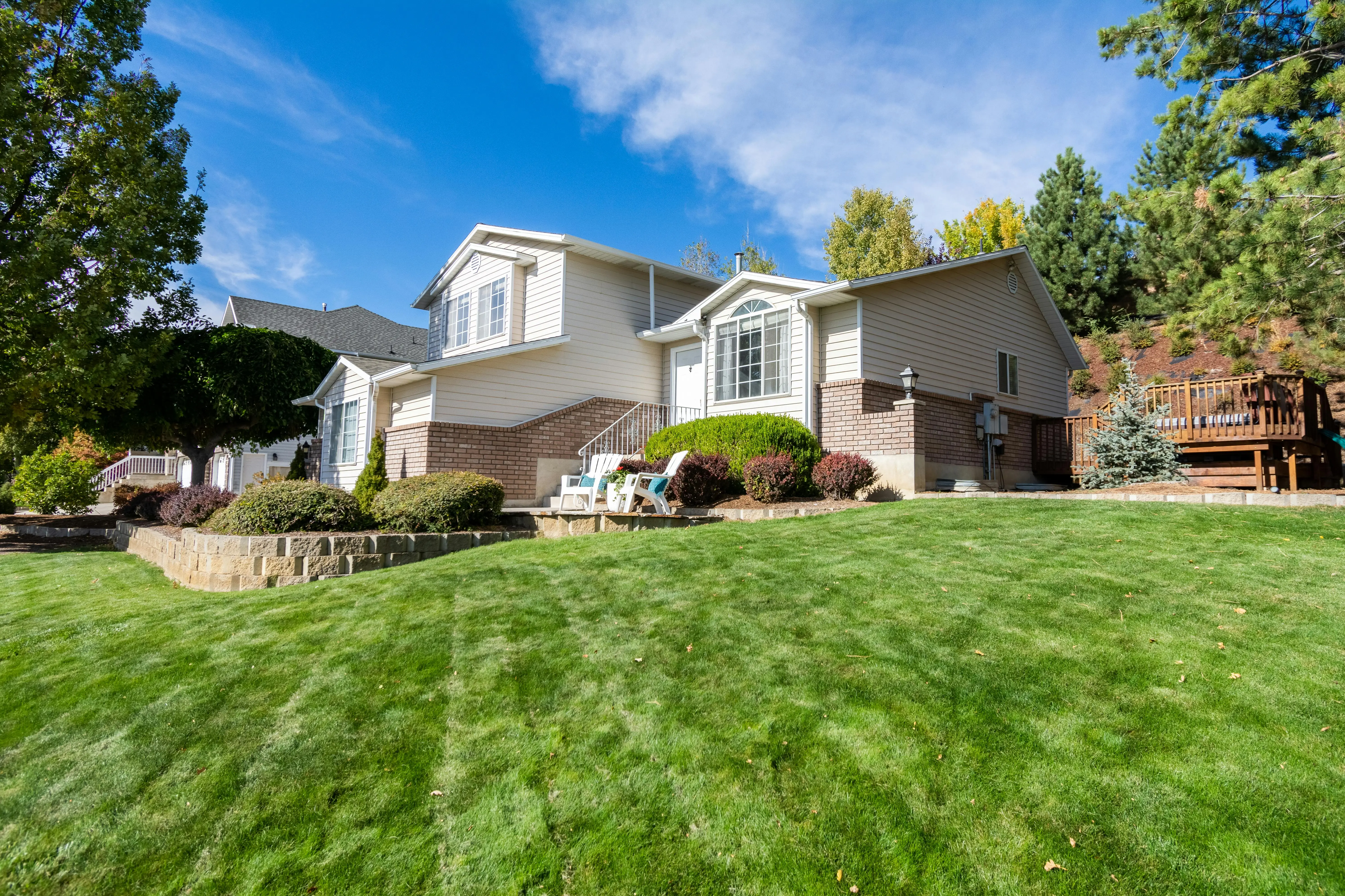 home addition cost Beautiful suburban house with a manicured lawn, framed by trees and blue sky.