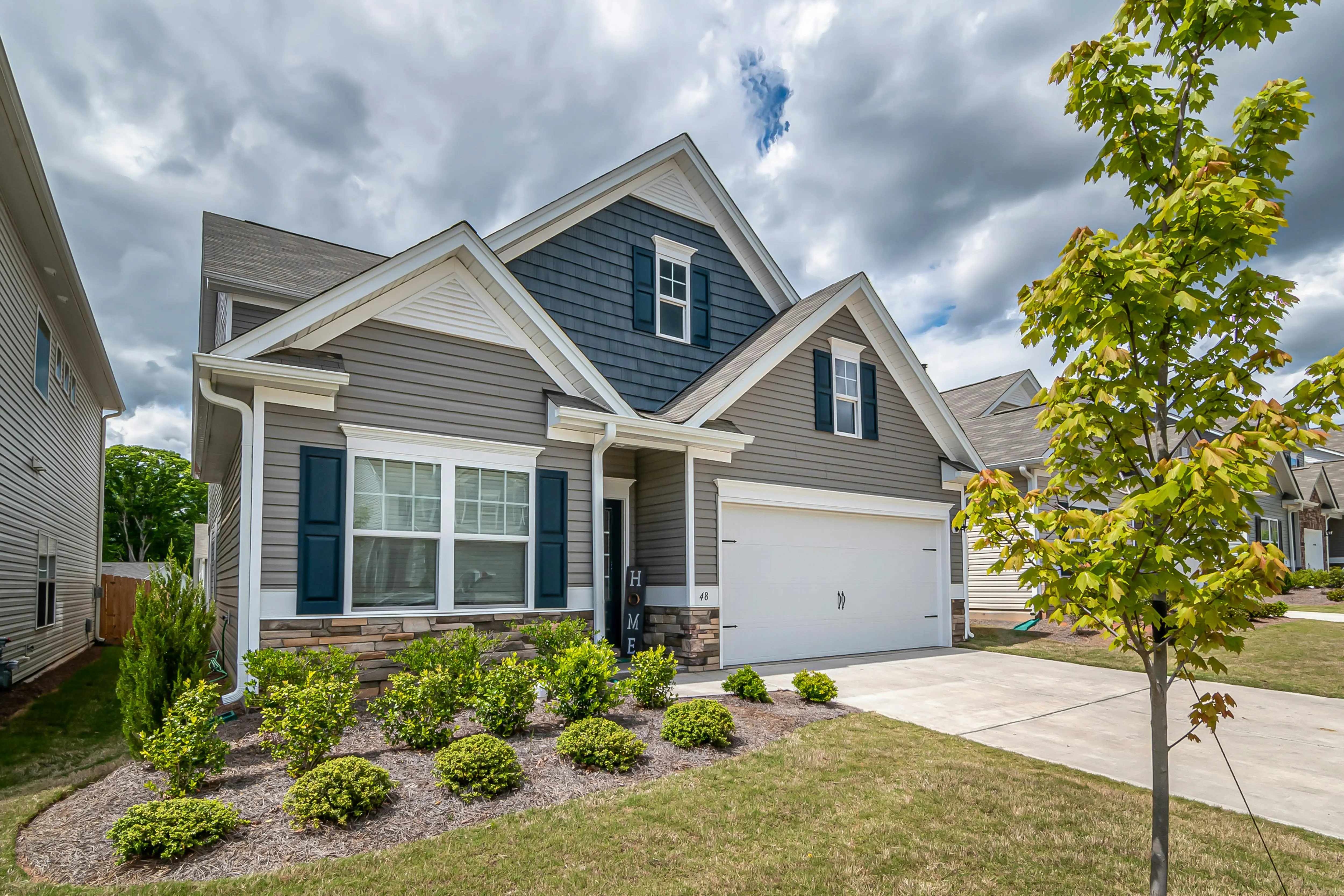 how much does it cost to side a house A beautiful suburban house with a manicured garden and cloudy sky, exemplifying modern architecture.