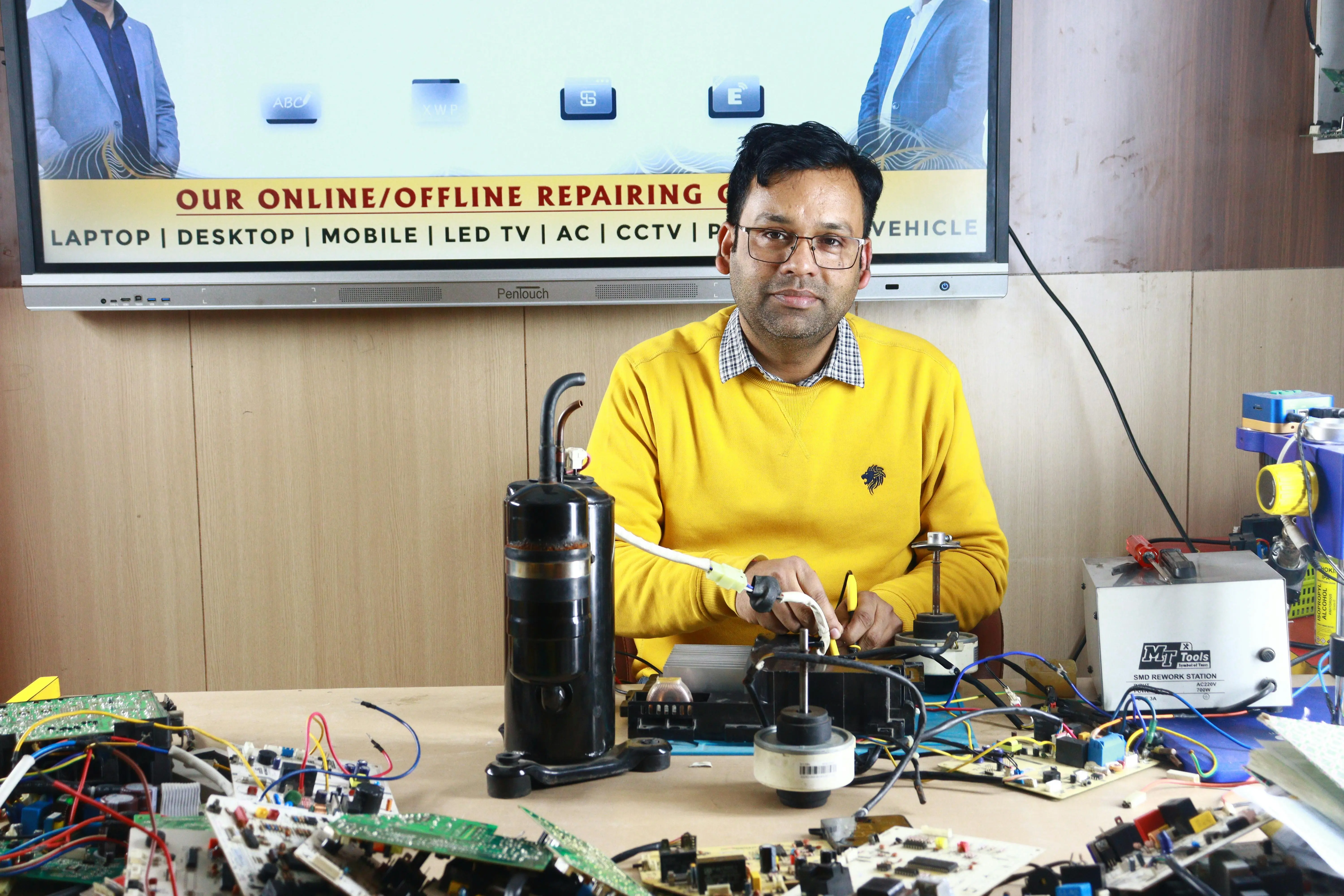how to clean evaporator coil Man engages in air conditioner repair at New Delhi training center, surrounded by electronic components.