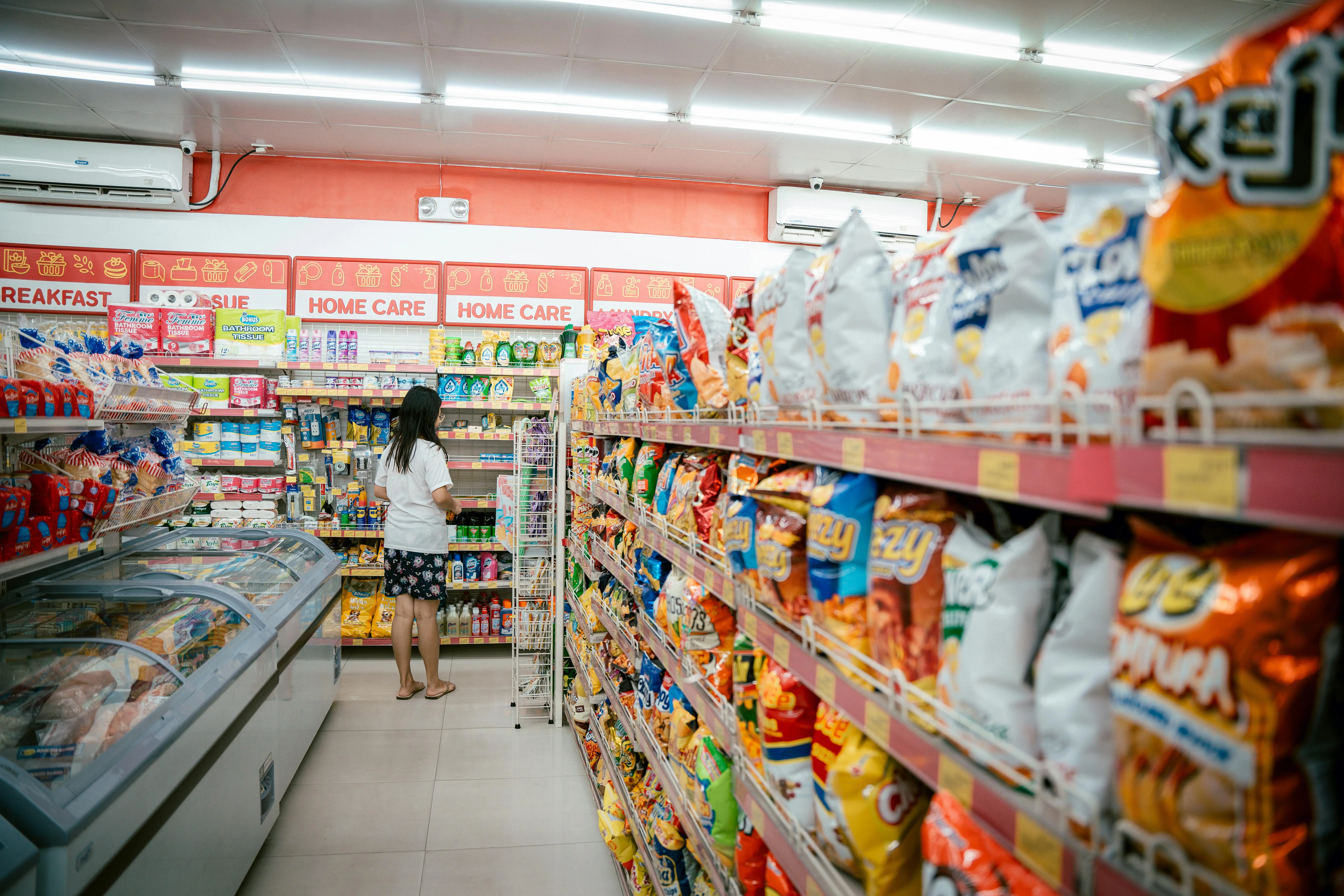 open box appliances A woman browsing snack shelves at a supermarket, surrounded by various chips packages.