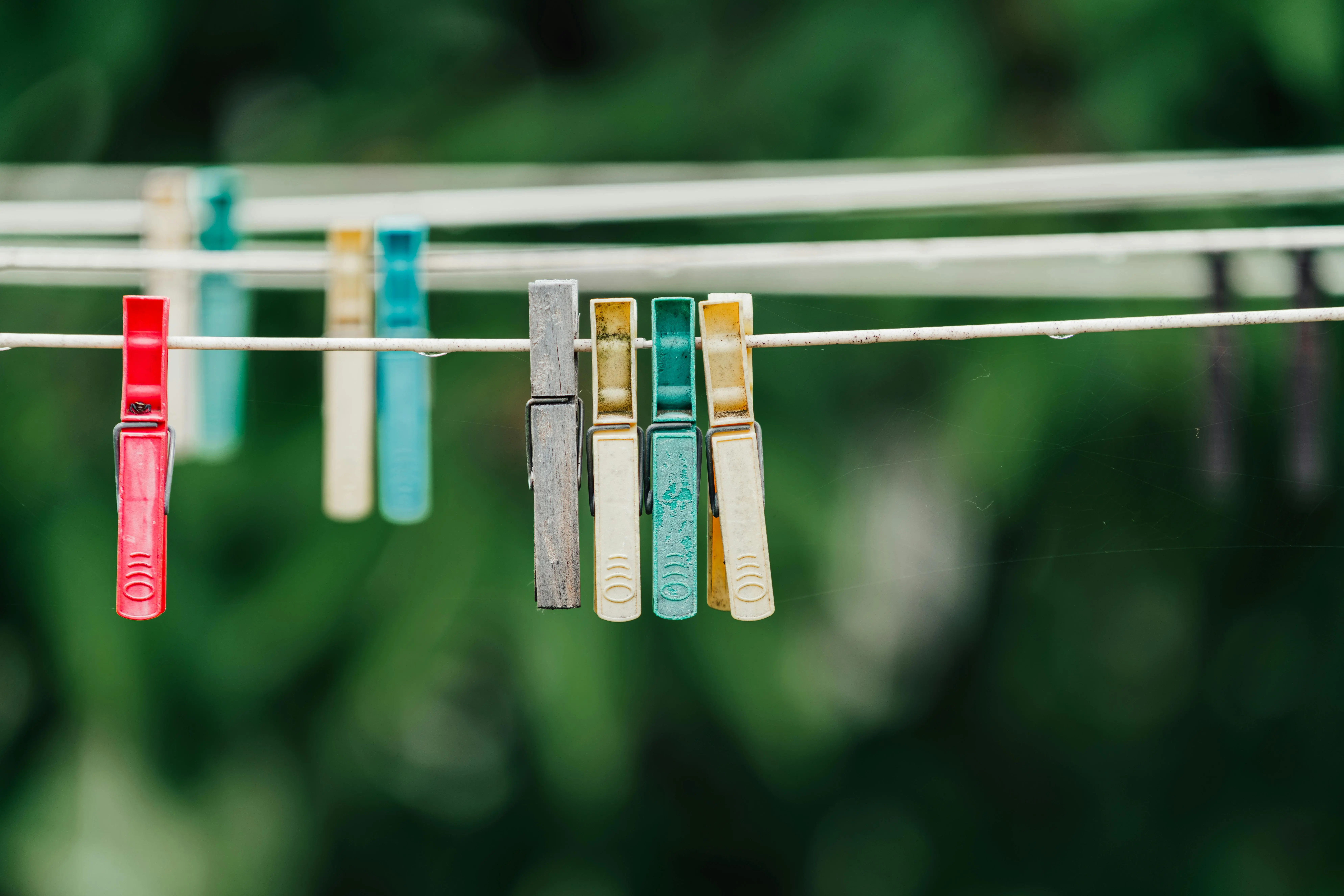 what can i use instead of laundry detergent Close-up of colorful clothespins hanging on a laundry line outside with a green backdrop.