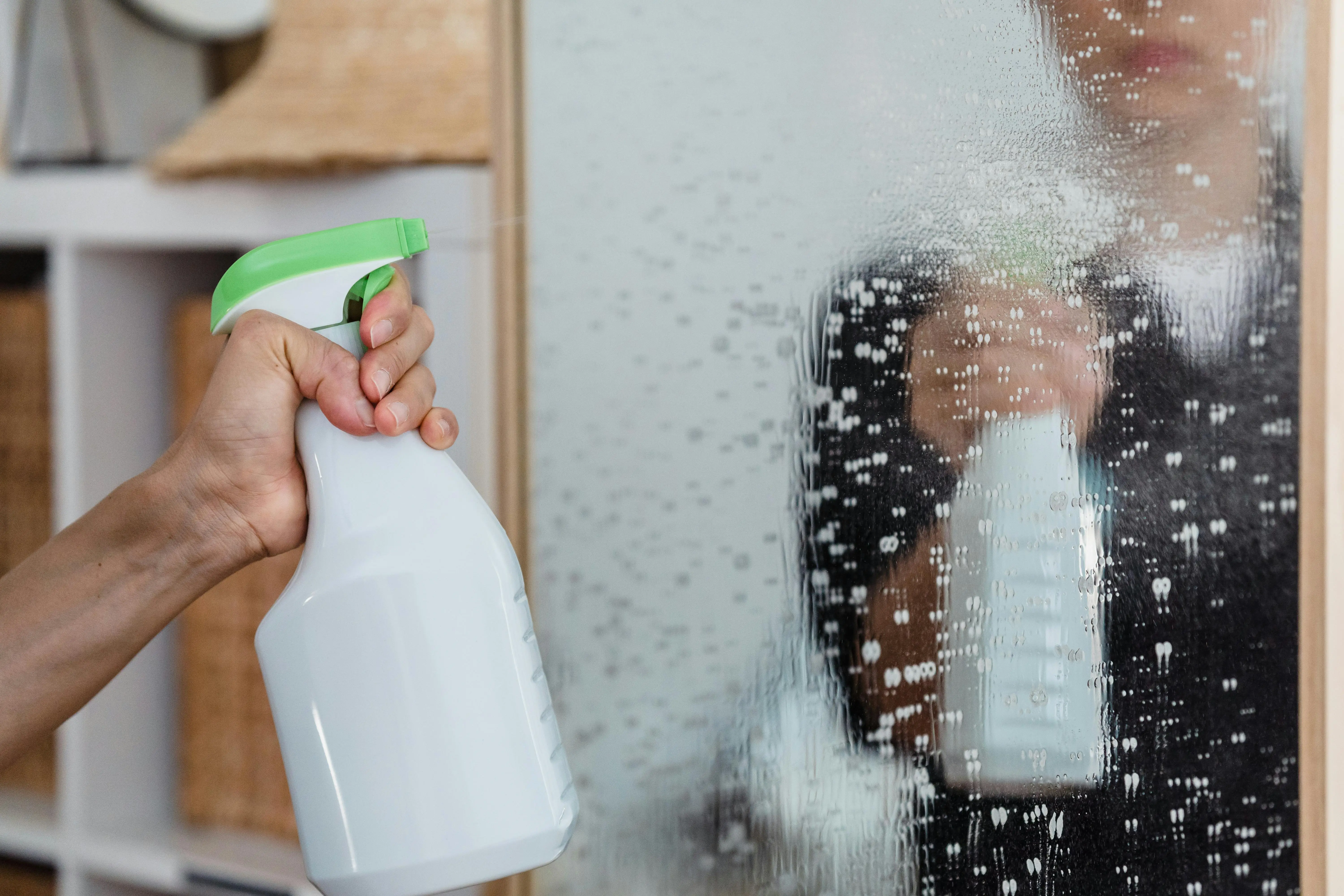 how to get urine smell out of clothes Close-up of a hand using a spray bottle to clean a mirror indoors.