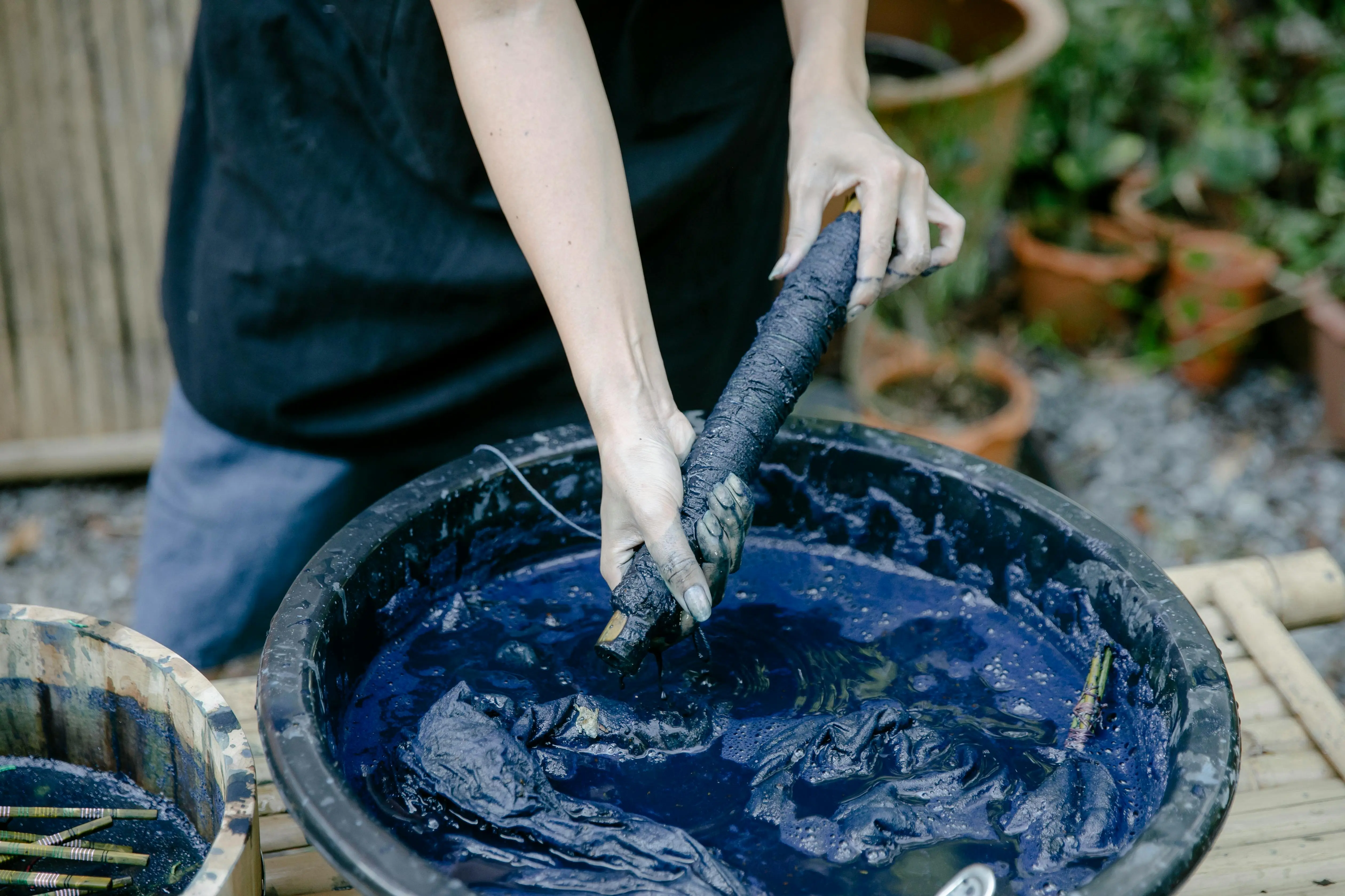 how to get rid of bleach stains A close-up of hands dyeing fabric with indigo dye outdoors, emphasizing traditional techniques.
