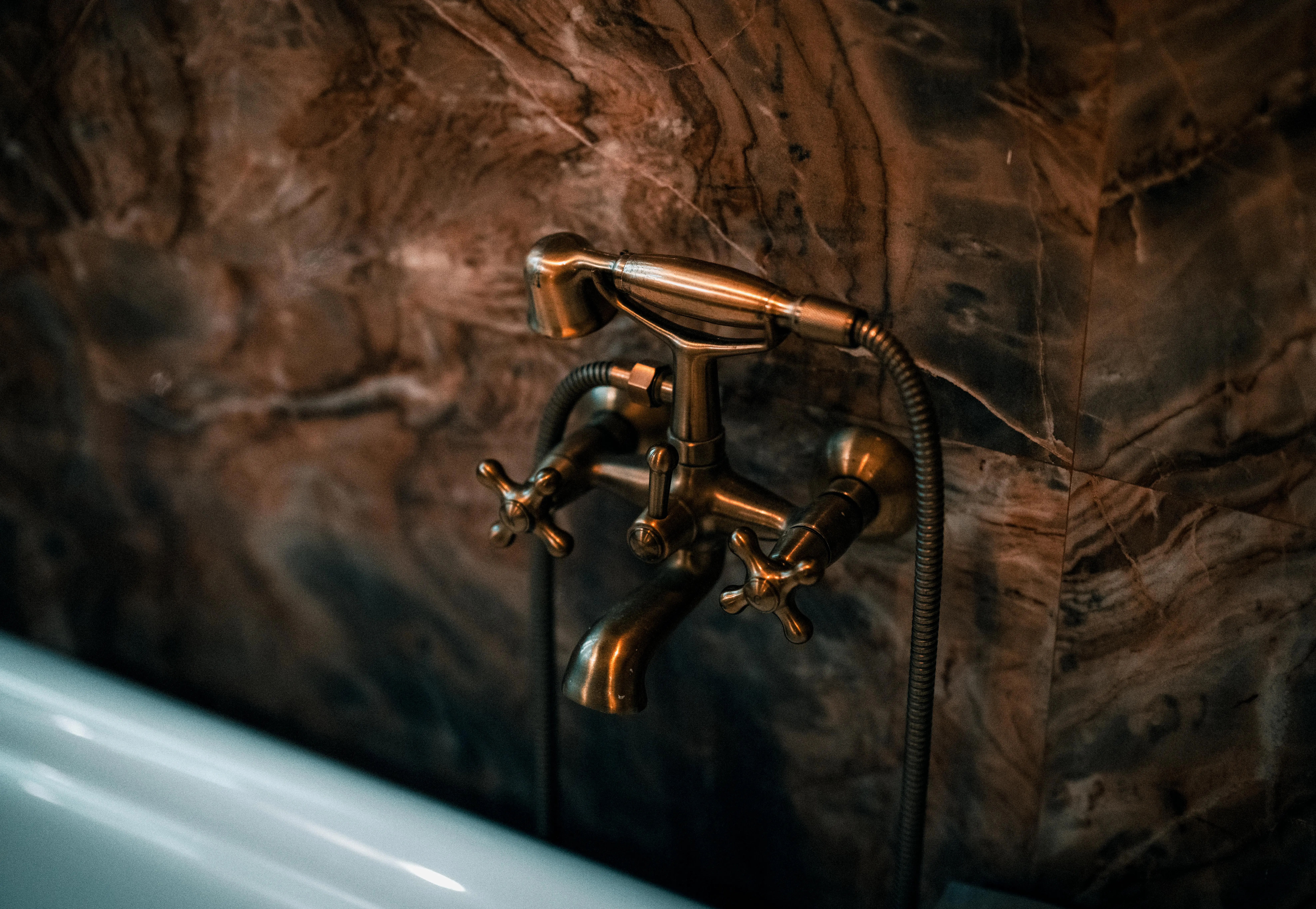 how to fix a leaky faucet single handle Elegant brass faucet fixture with a luxurious marble wall background.