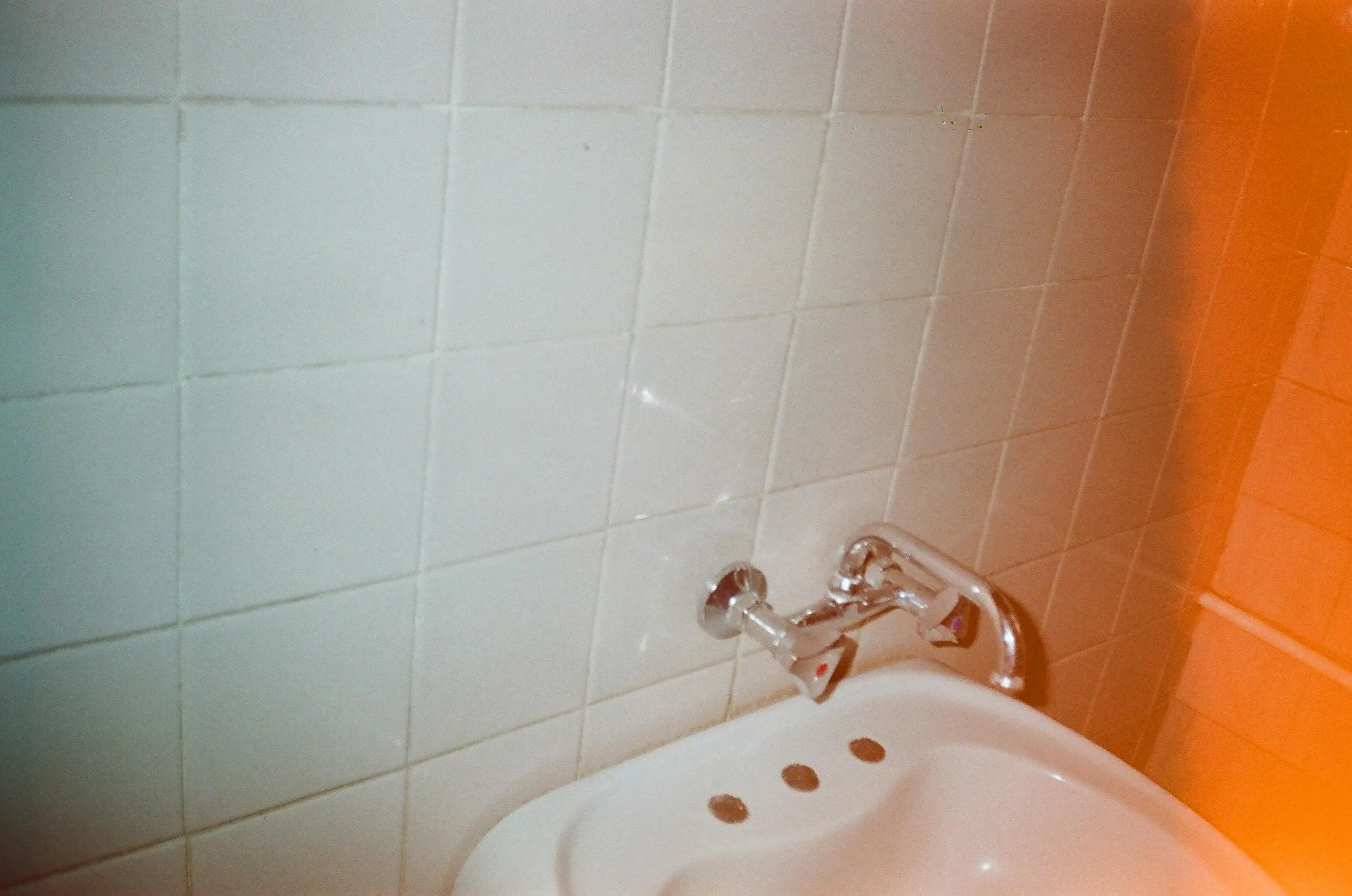 how to fix a leaky faucet single handle A simple white tiled wall with a classic ceramic sink and chrome faucet in a bathroom setting.