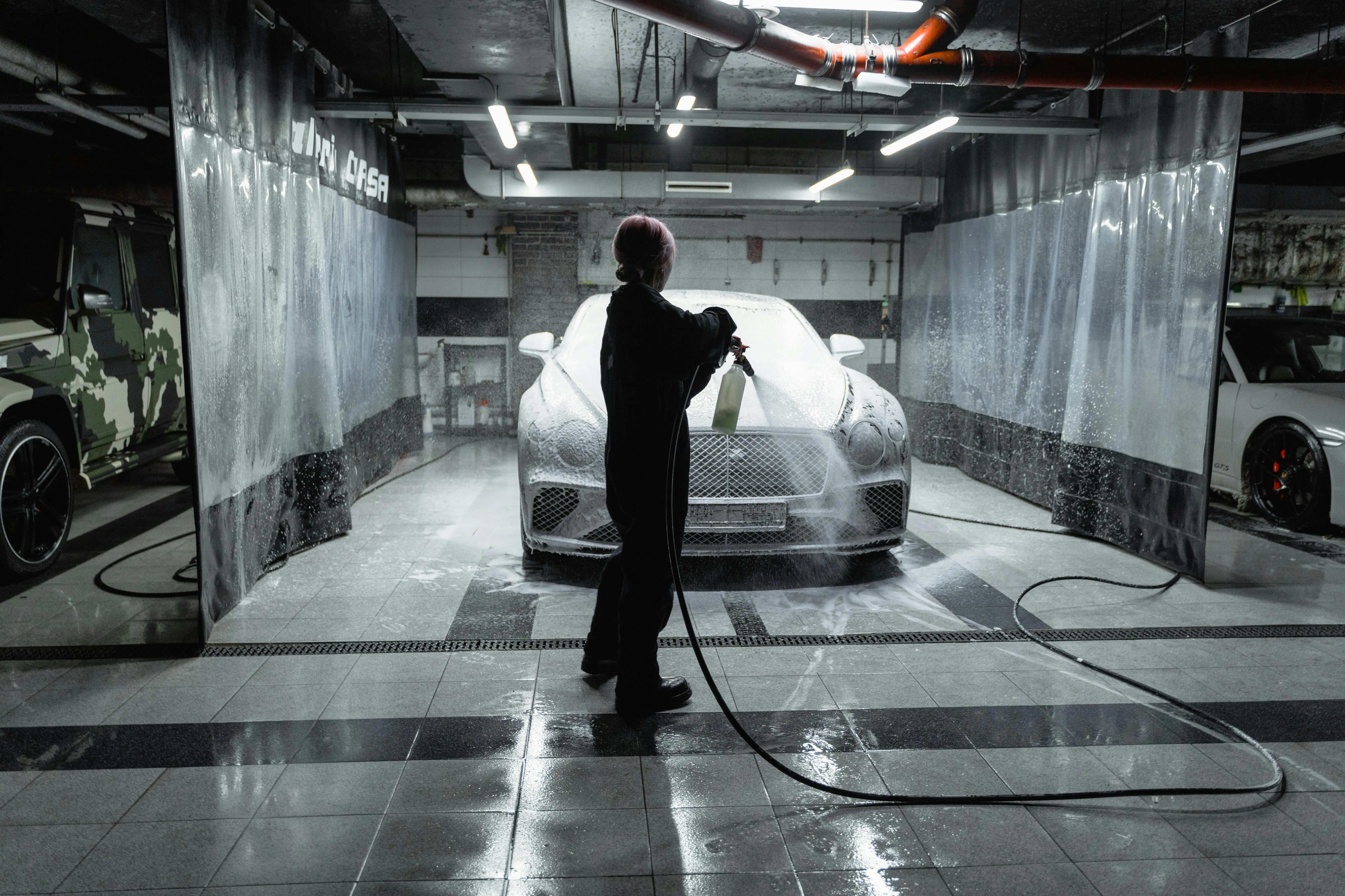 diy garage floor coating A person using a hose to spray a car with snow foam in an indoor carwash setting.
