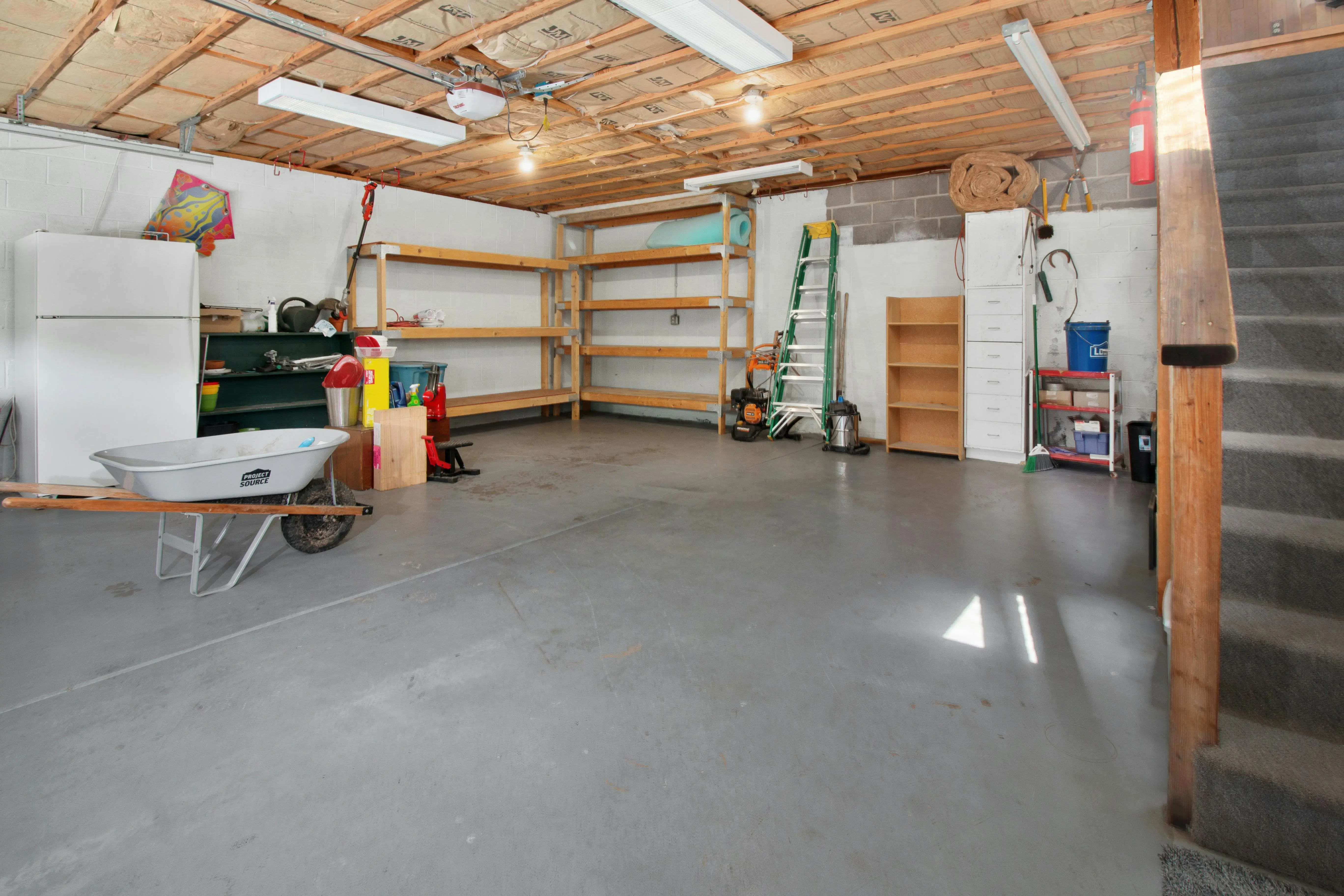 diy garage floor coating Spacious garage interior with storage shelves, tools, and a wheelbarrow, ideal for home organization.