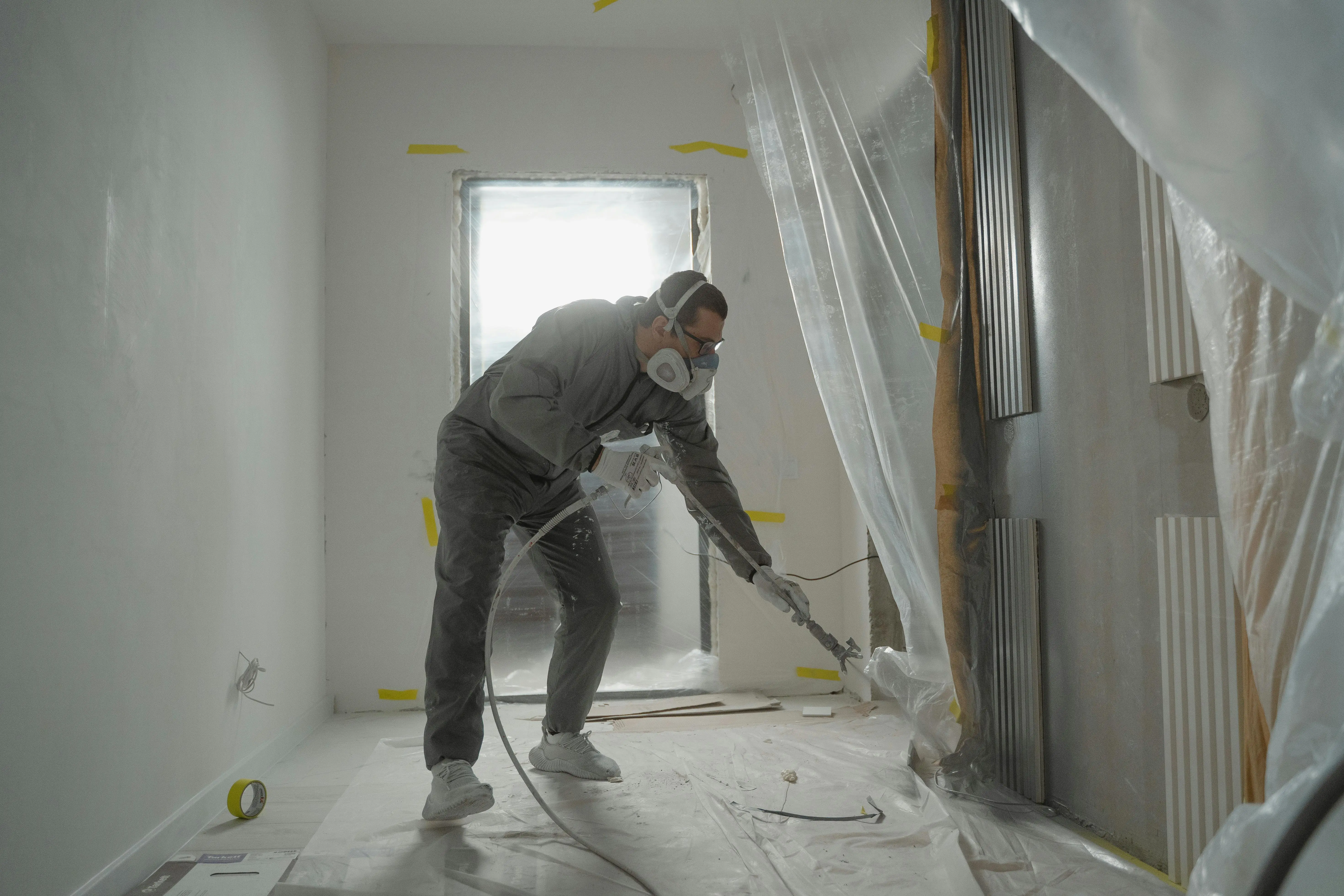 how much does a handyman charge to paint a room A worker in protective gear painting walls during an indoor renovation project.
