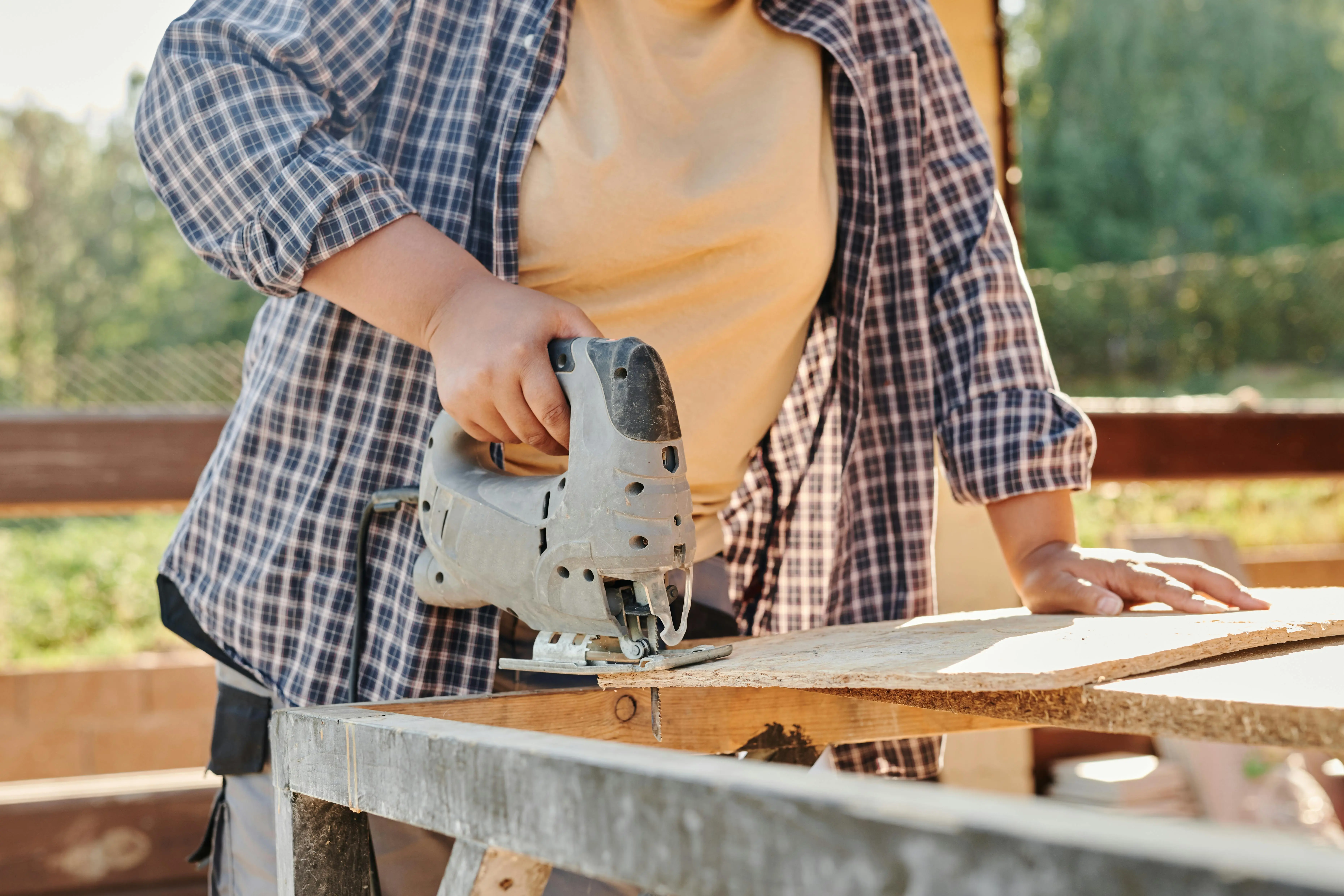 how to cut laminate flooring A carpenter using a jigsaw to cut plywood at a construction site. Outdoor setting.