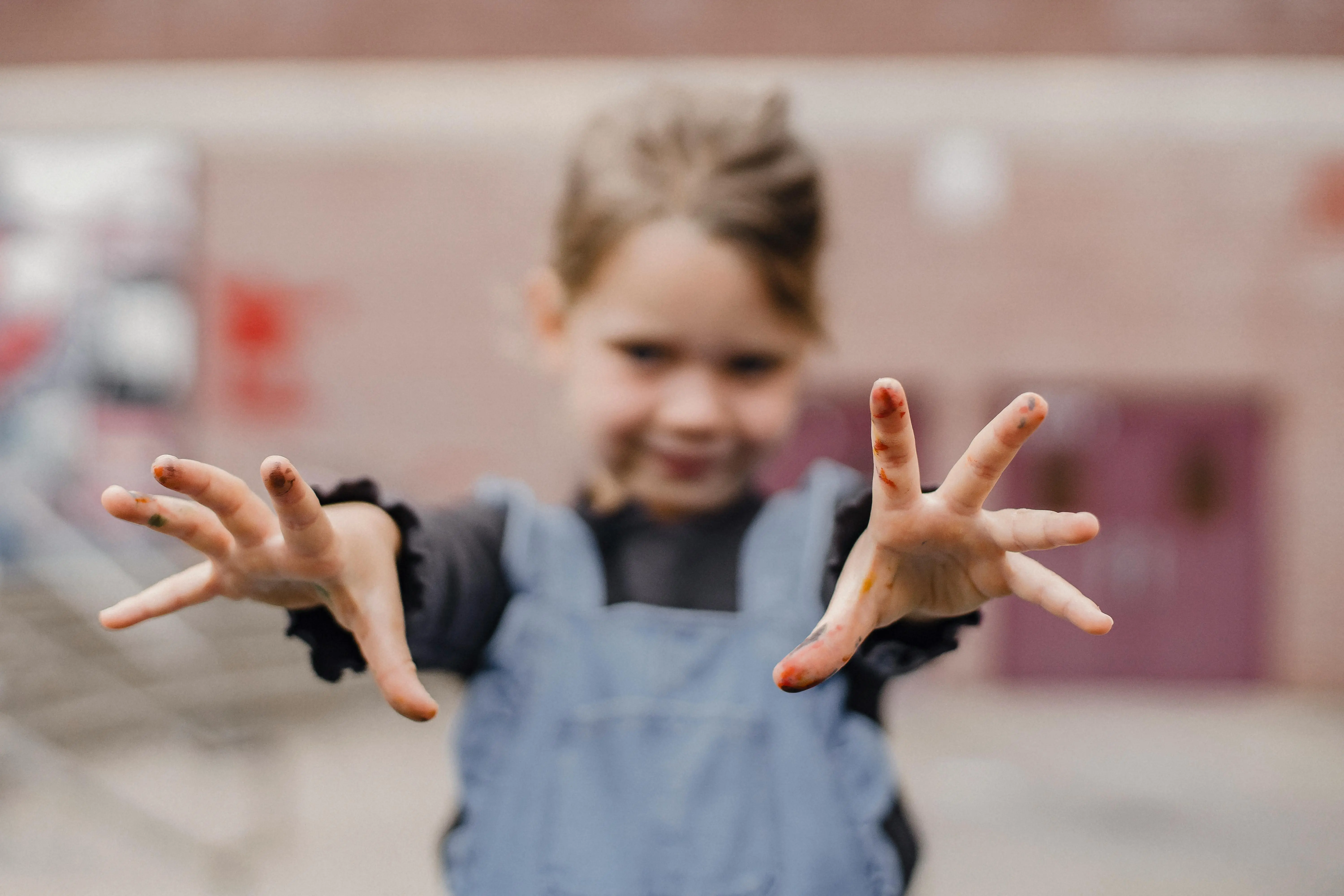 crafts for pre k Adorable little girl in casual clothes with painted fingers outstretching arms towards camera while drawing in kindergarten