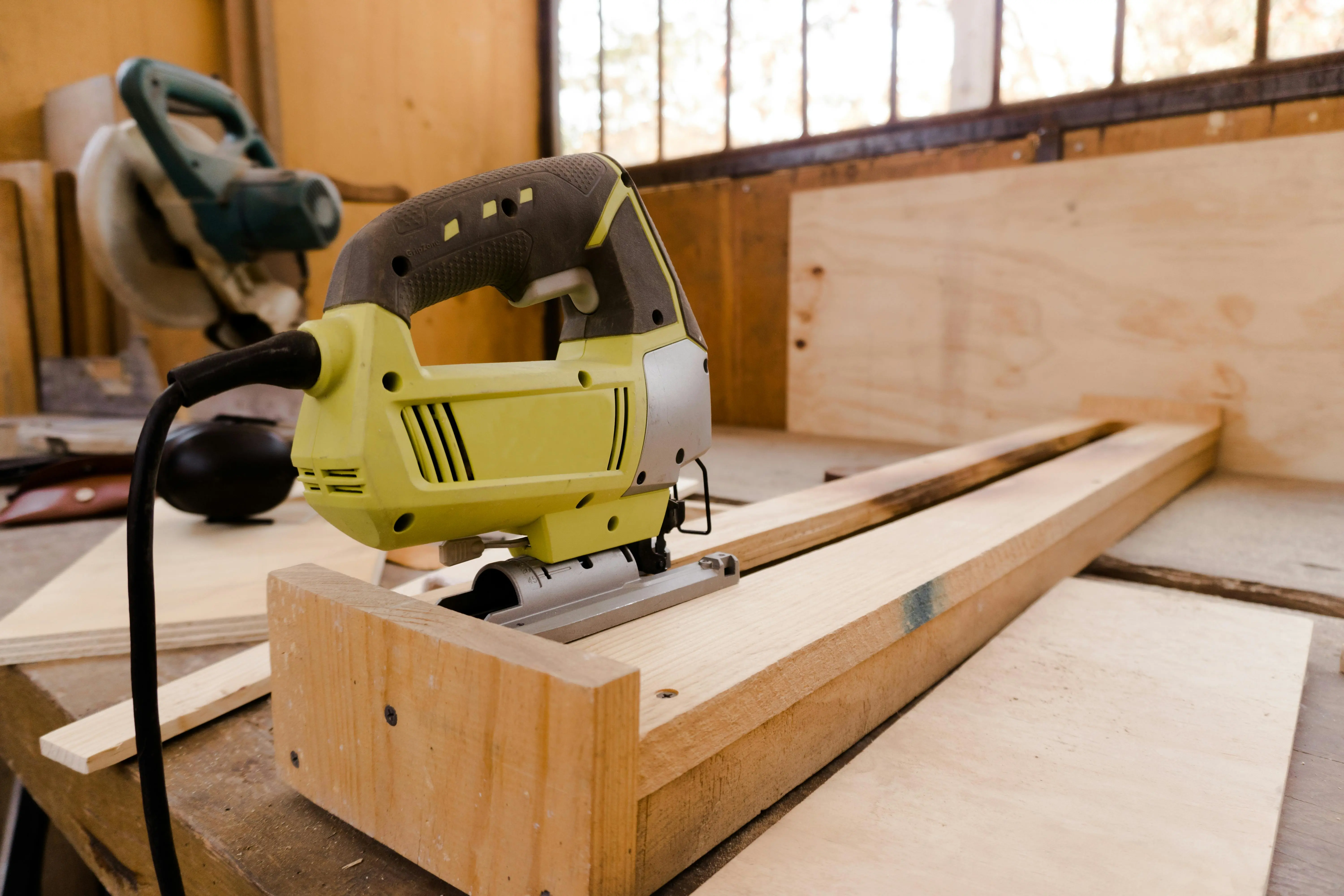 how to cut laminate flooring A close-up of an electric jigsaw placed on a wooden workbench in a carpentry workshop.