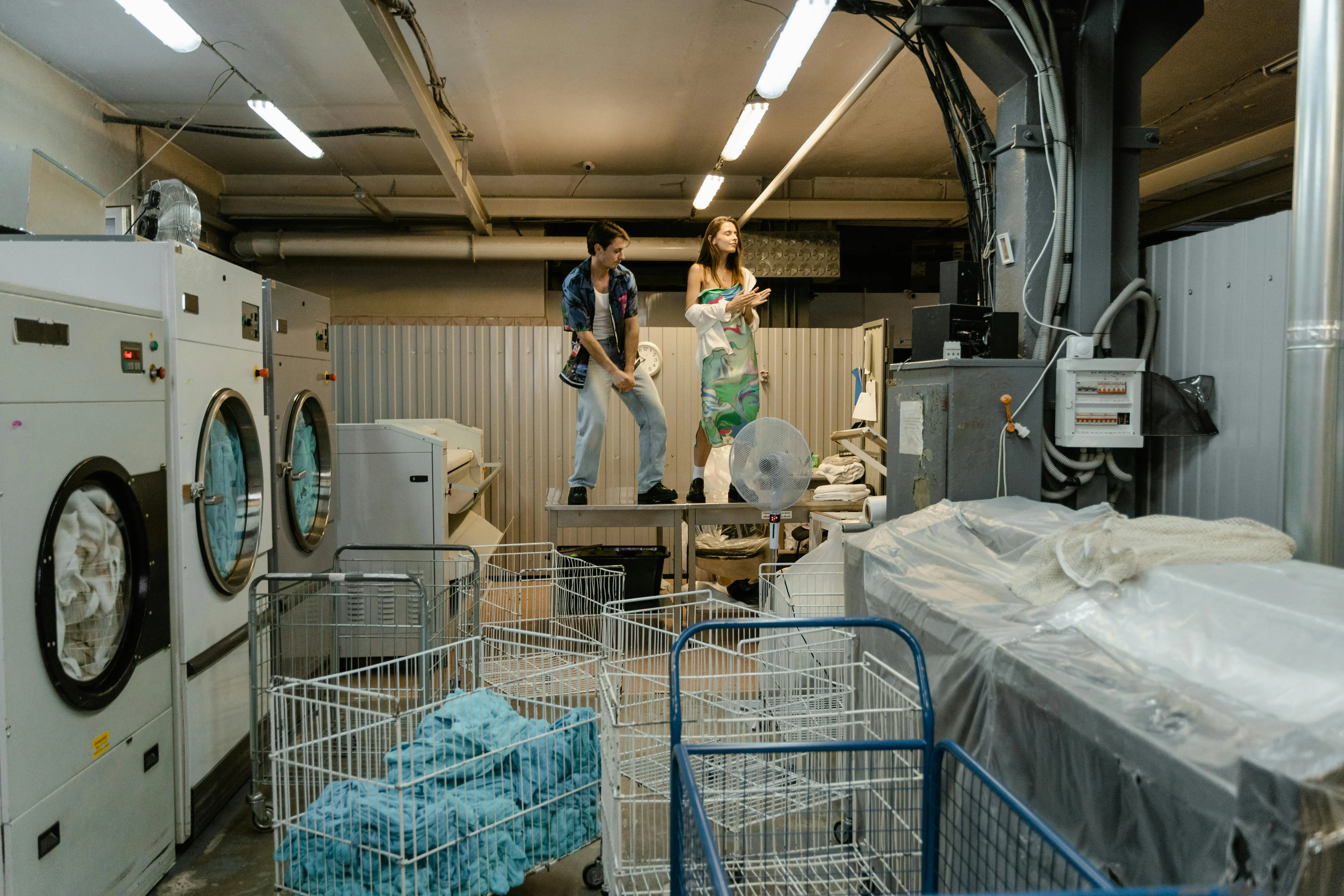 how to get tree sap out of clothes Two people take a break in a busy industrial laundry facility, surrounded by machines and laundry carts.