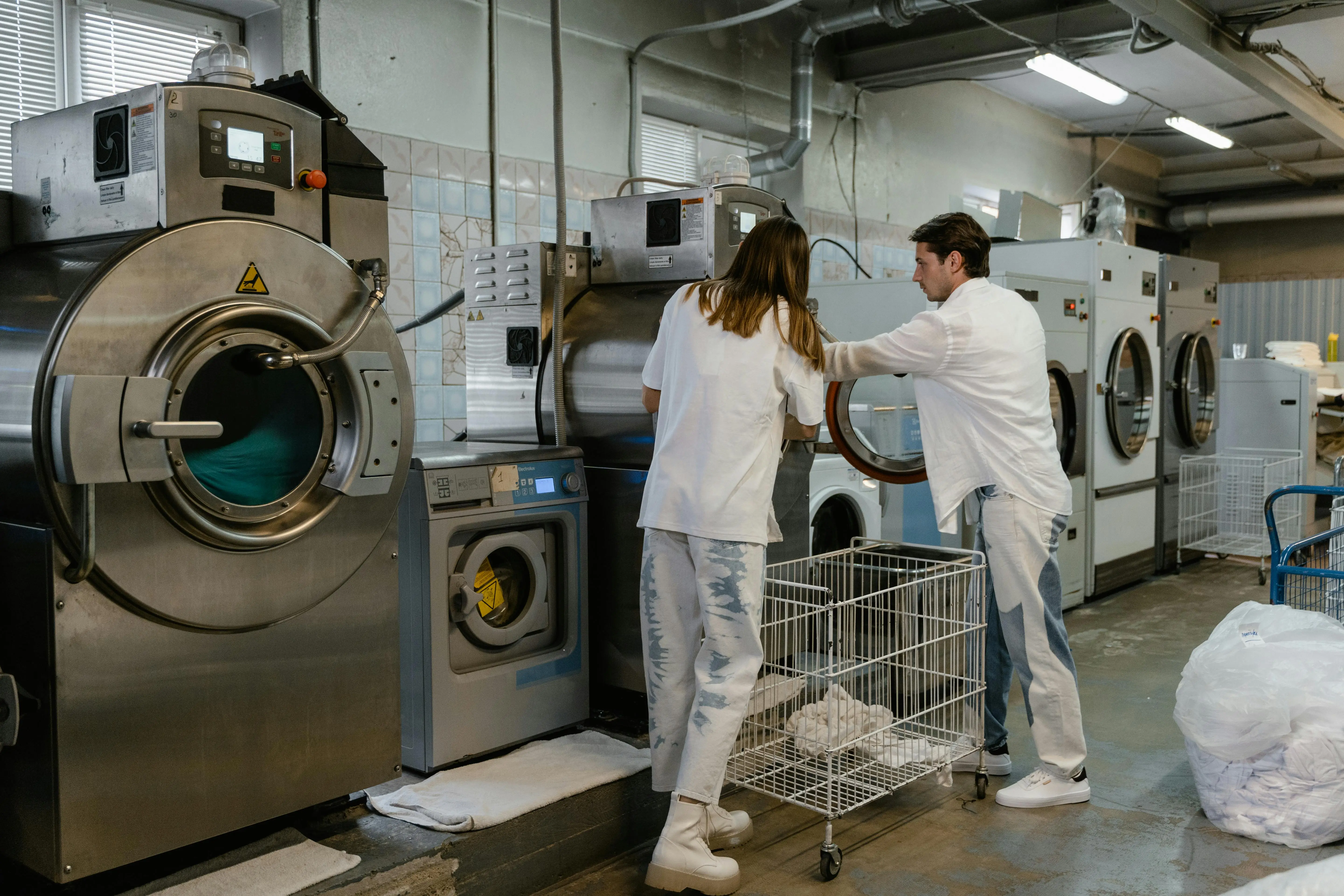 open box appliances Two adults working in an industrial laundry facility with large machines.