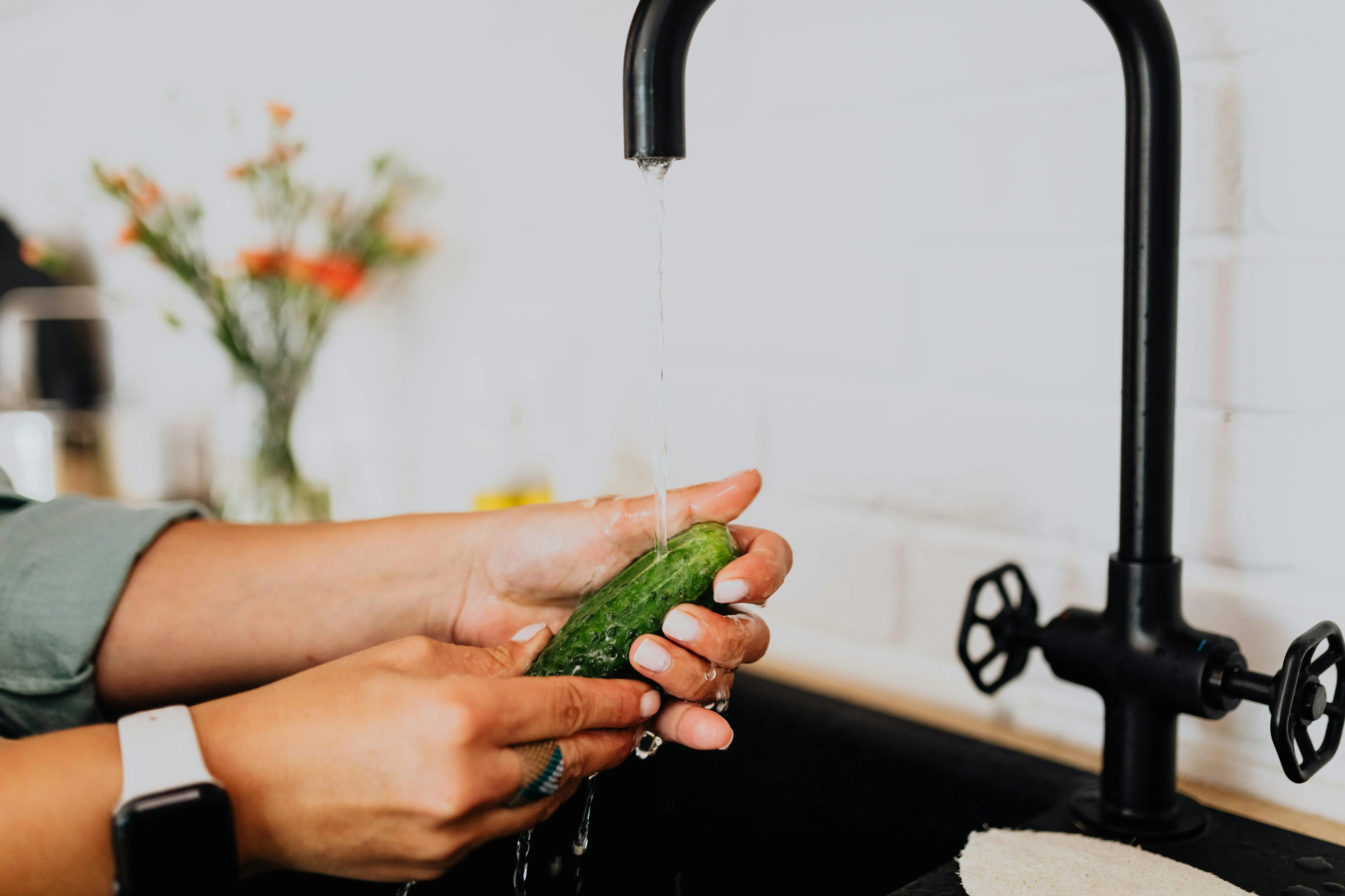 get rid of calcium deposit marks sink Hands washing a fresh cucumber under running water in a kitchen setting.