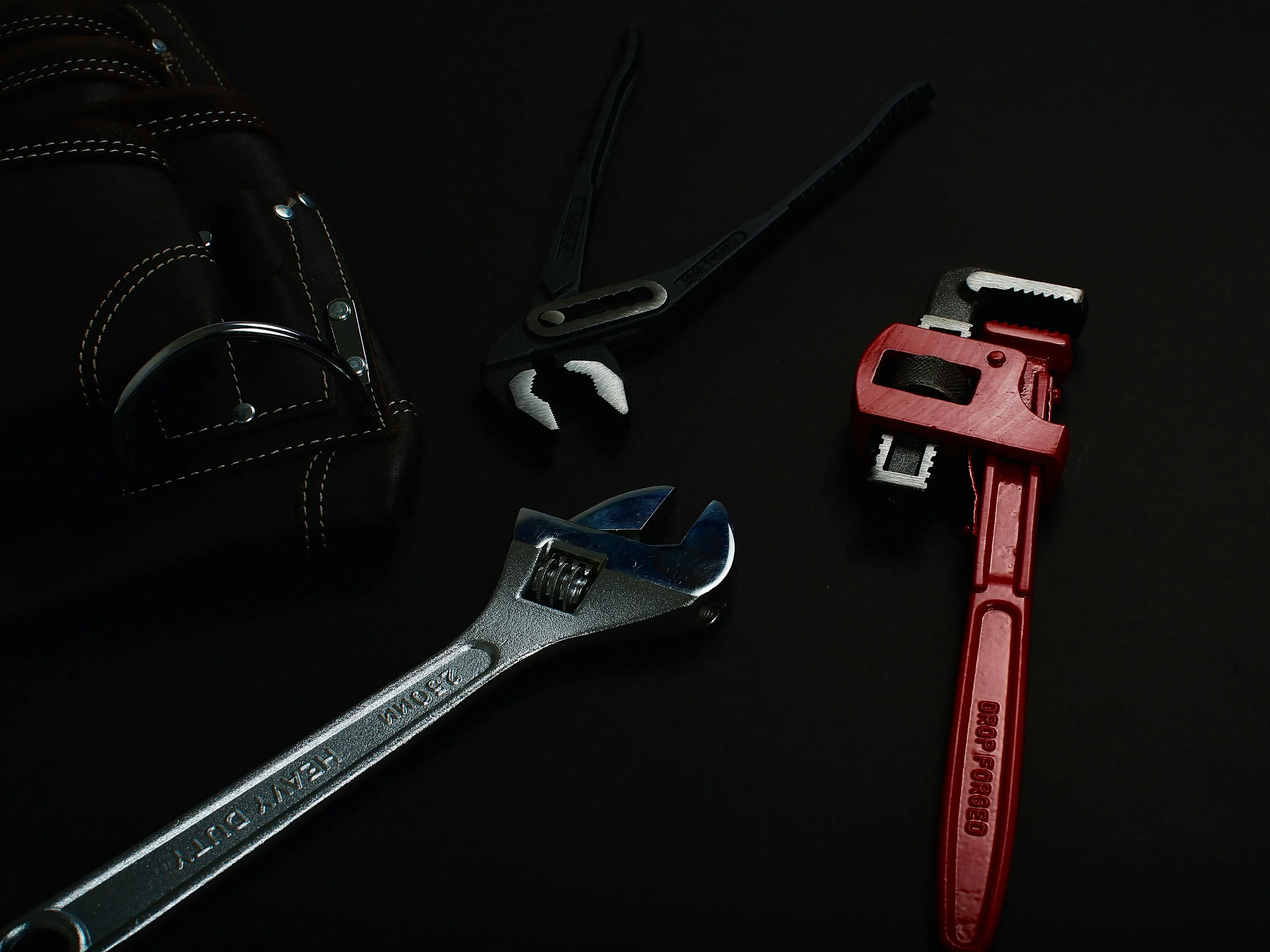 how to fix a leaky faucet single handle Close-up of various hand tools including wrenches and pliers on a dark surface.
