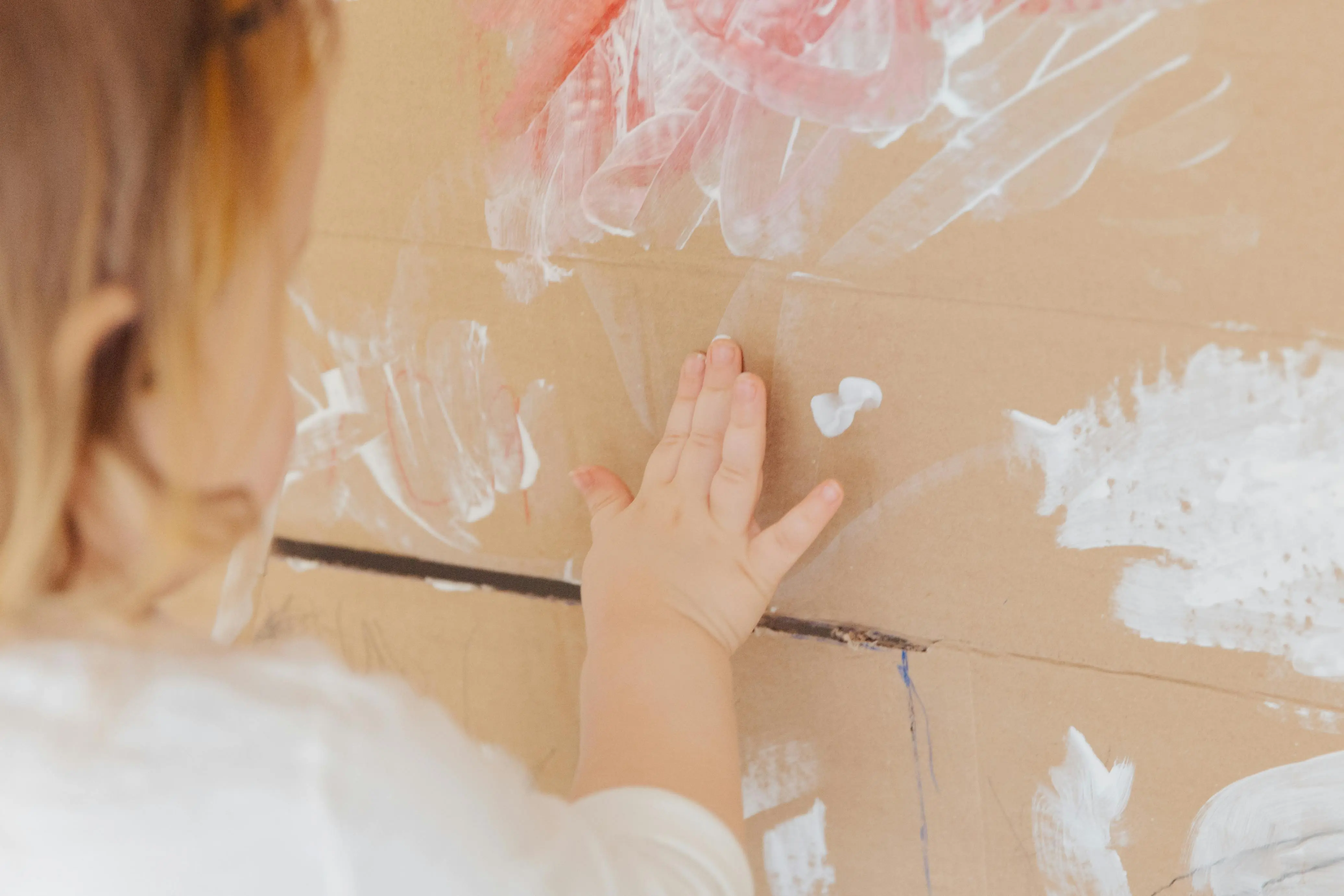 crafts for pre k Back view of crop faceless child smearing white paint with fingers on beige surface at home
