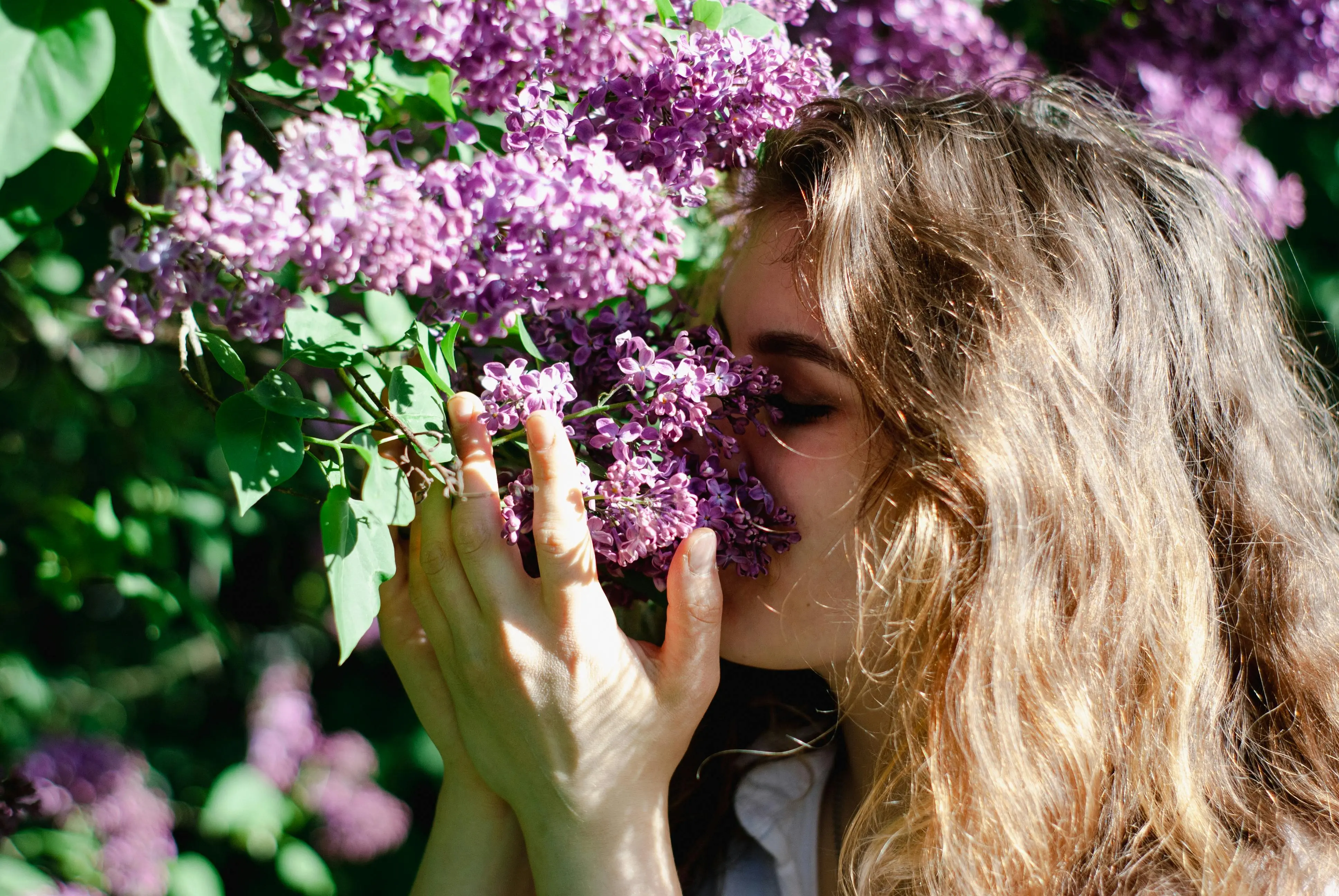 how to get rid of mildew smell in clothes A young woman relishes the scent of lilac flowers in a sunlit garden, embodying spring and relaxation.