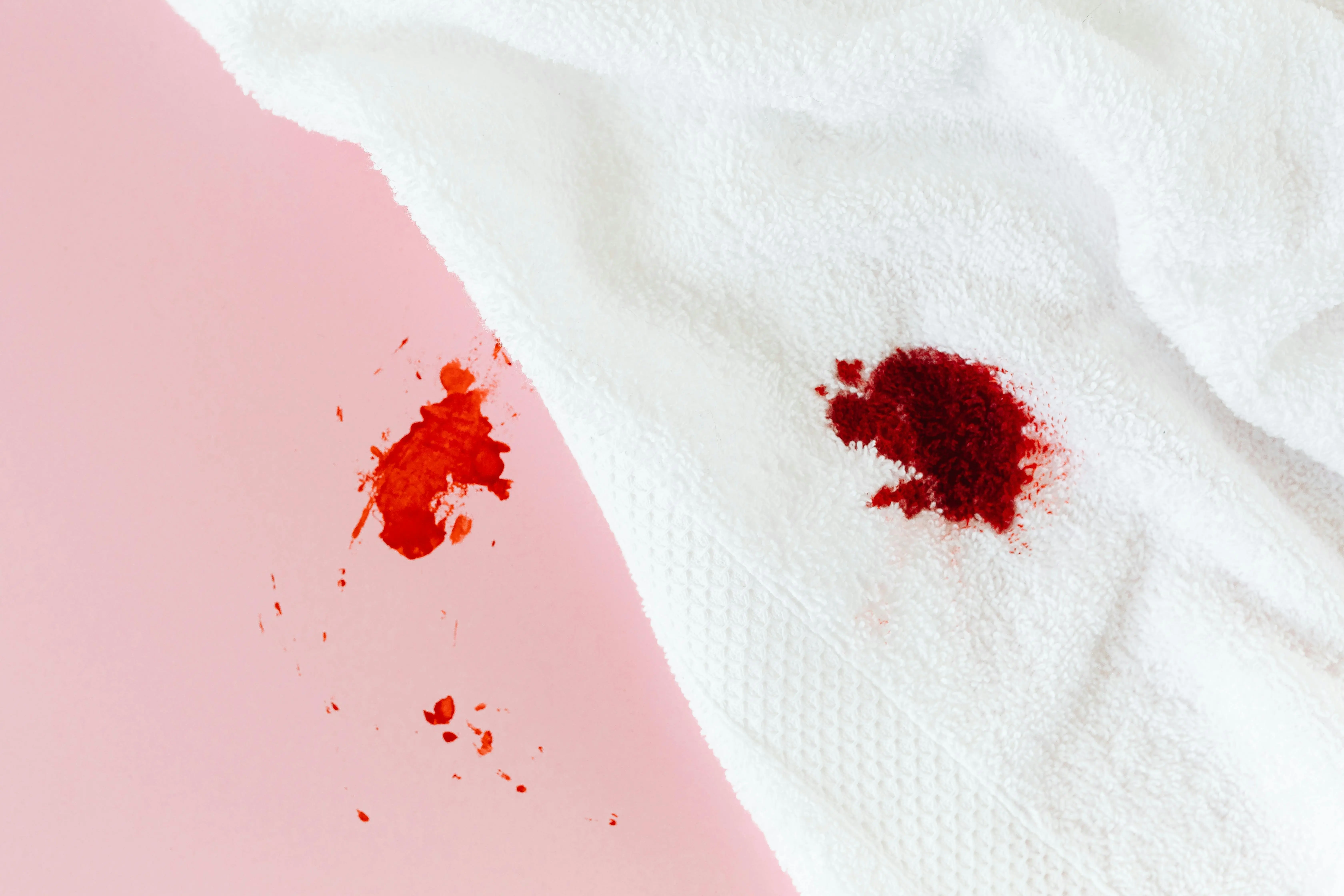 how to get motor oil out of clothes Red blood stain on a white towel spread over a pastel pink background, close-up shot.