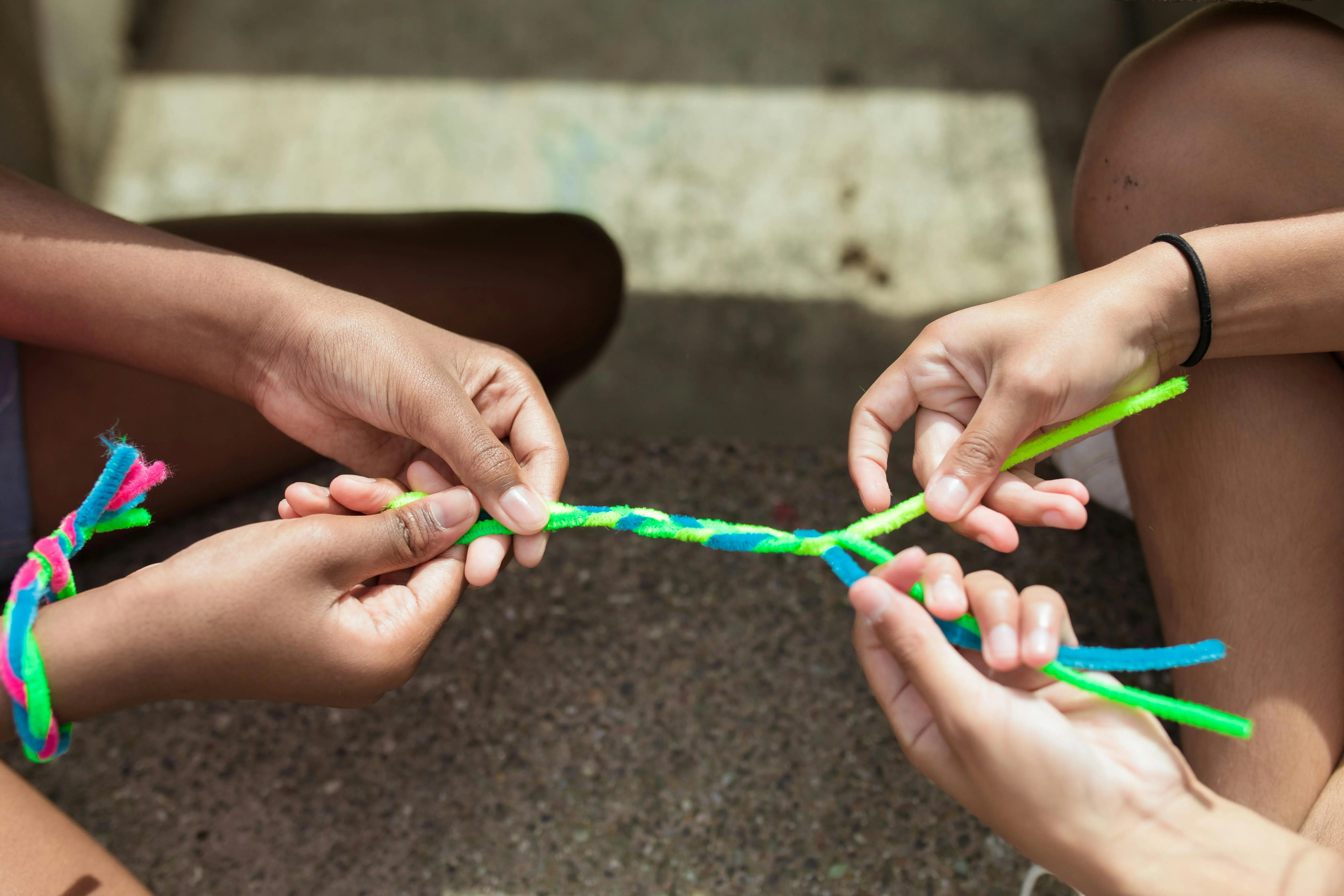 crafts for pre k Close-up of kids making vibrant yarn bracelets at summer camp, focusing on hands and creativity.