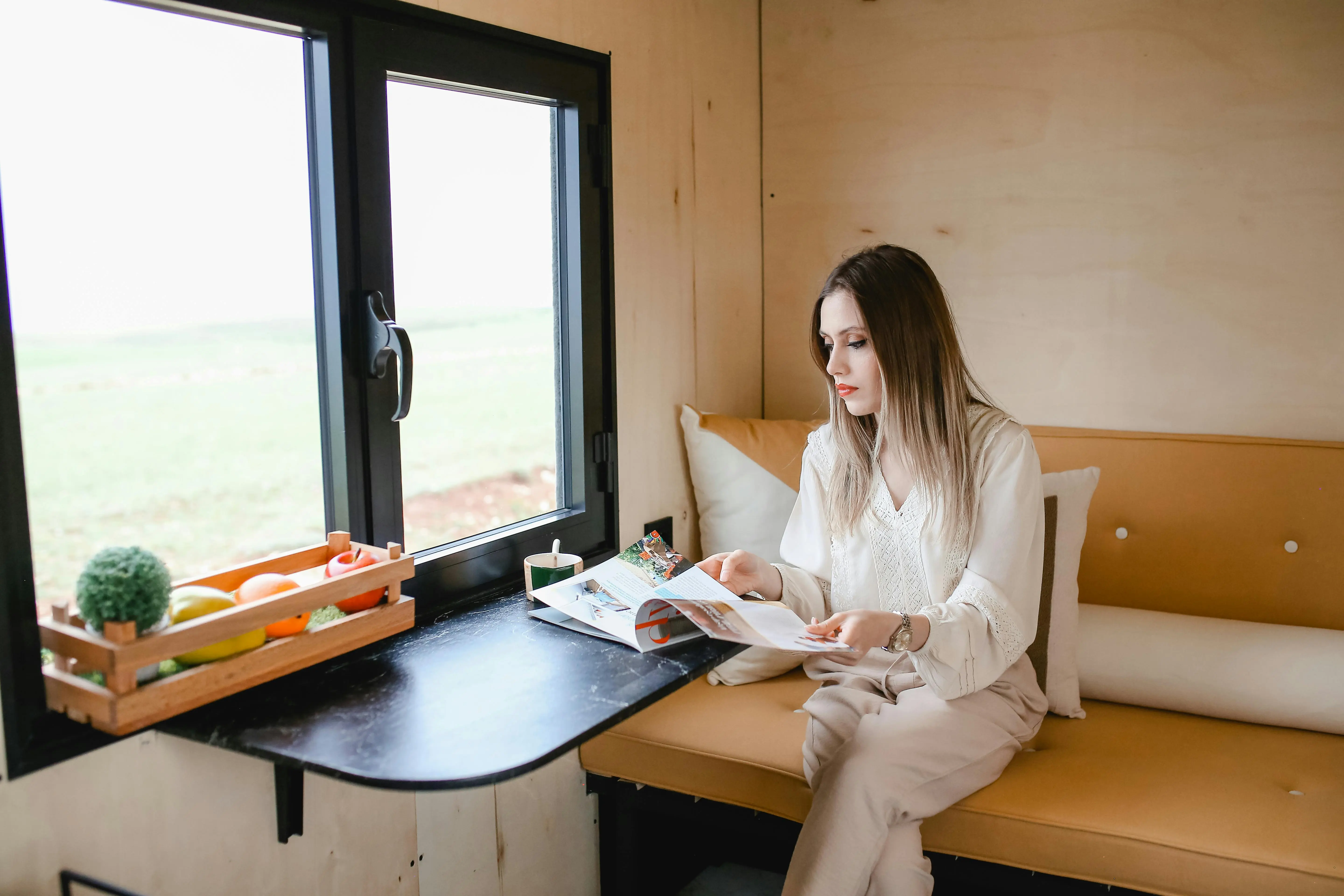 tiny house movement california Woman reading magazine in a cozy tiny house with a scenic view.