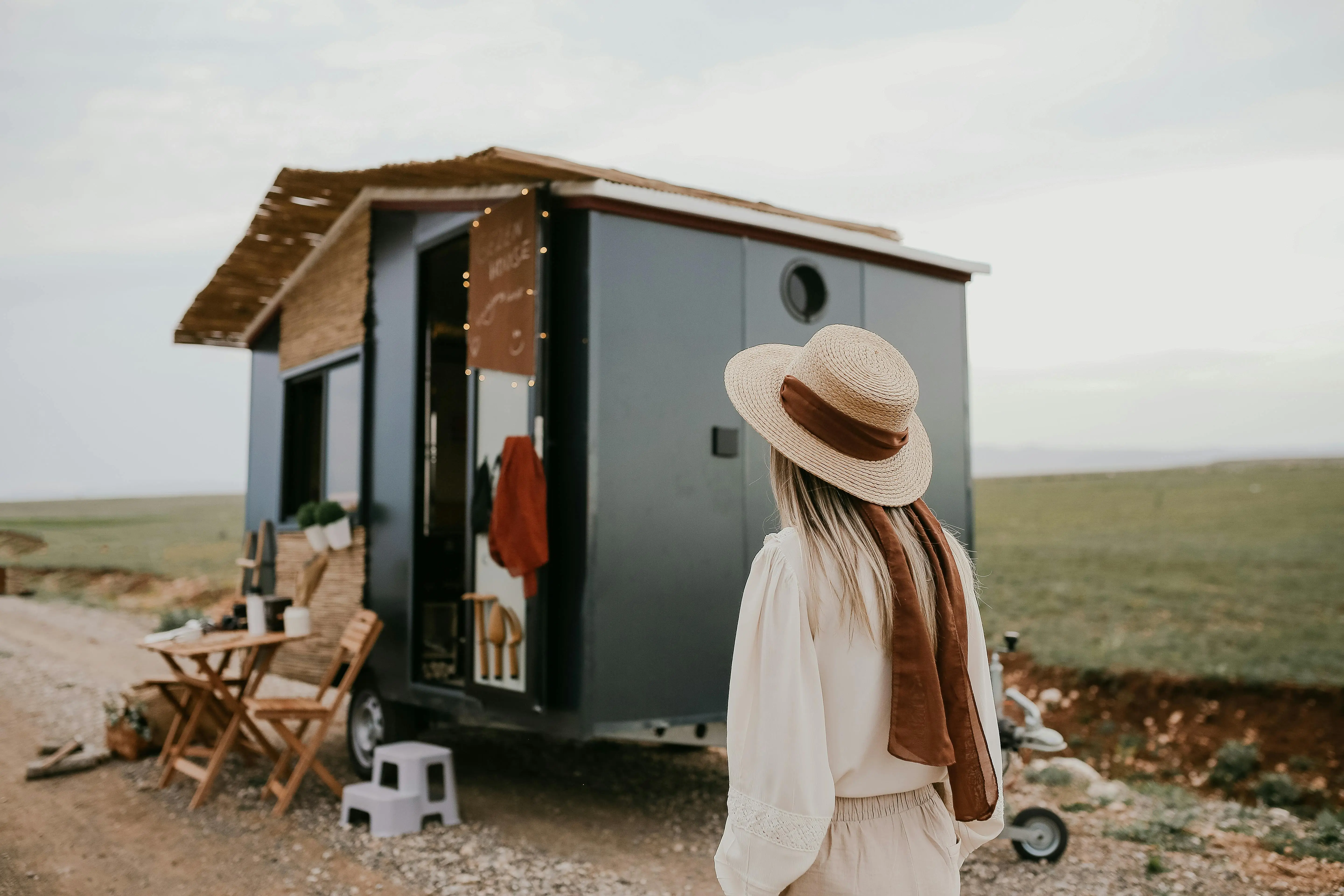 tiny house movement california Woman standing by a tiny house on wheels in a rural landscape, capturing the essence of mobile living.