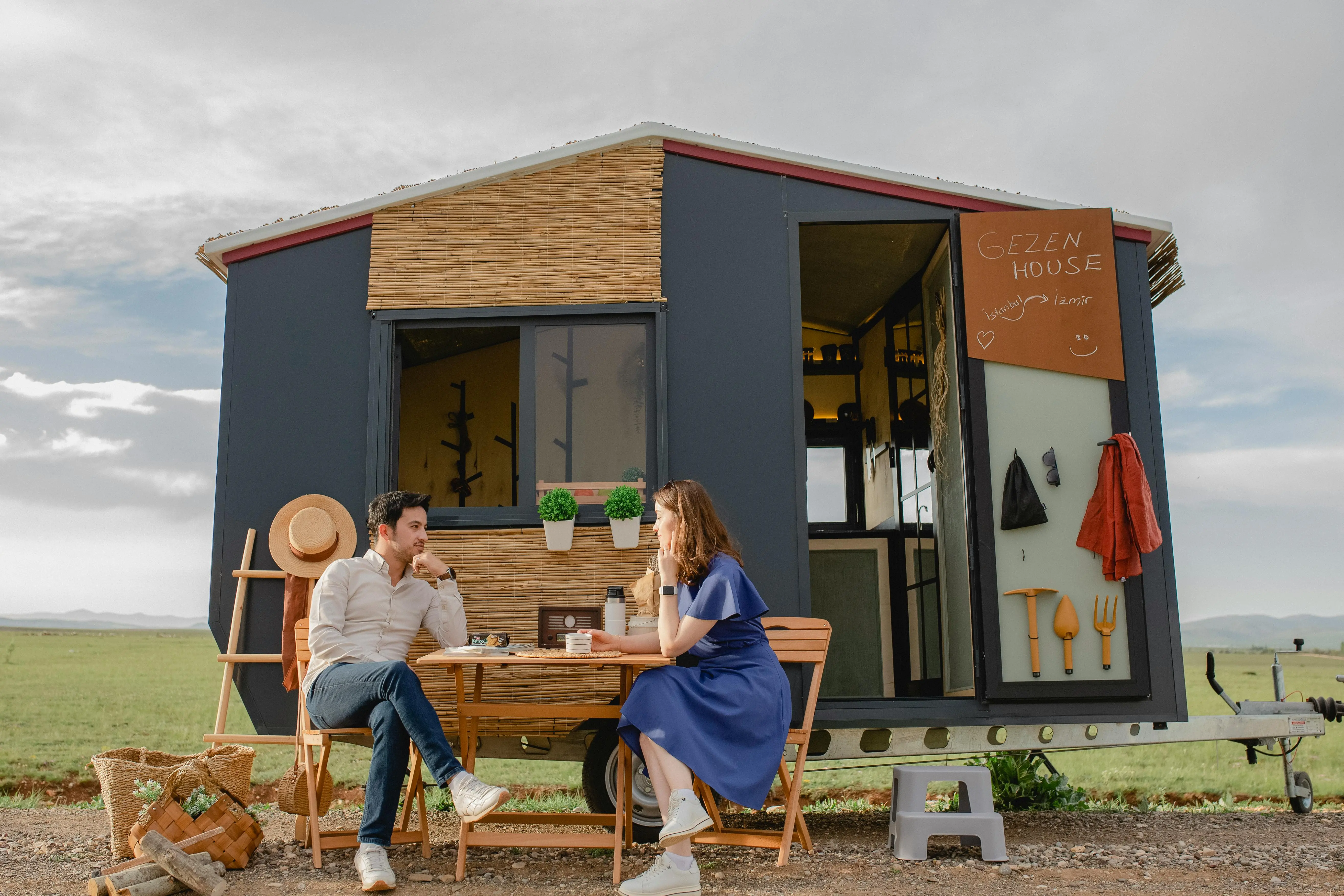 tiny house on foundation A young couple relaxing at a picnic table outside a modern tiny home in nature.
