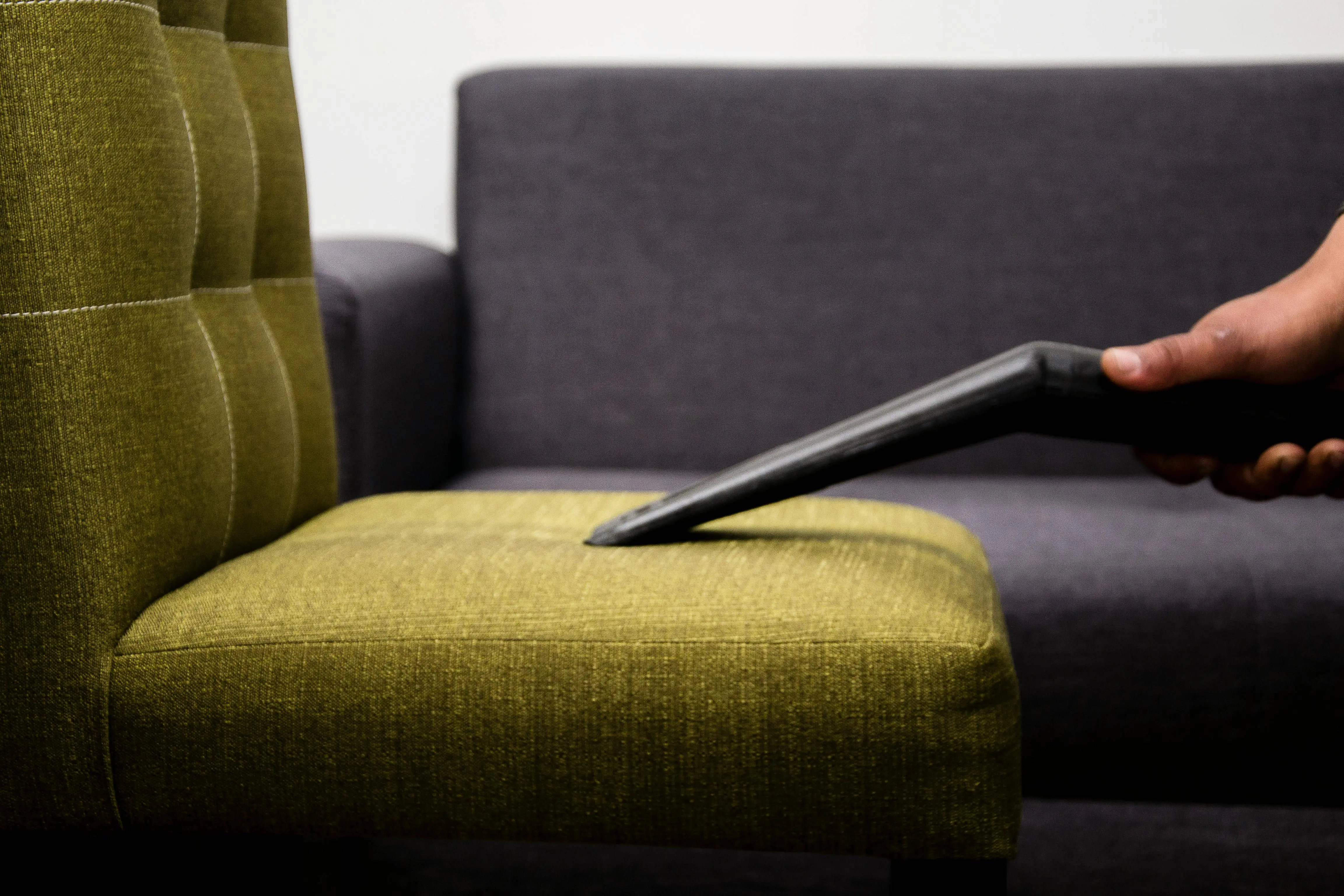 how to clean upholstered furniture Close-up of a person vacuuming a modern sofa chair indoors, highlighting cleaning service.