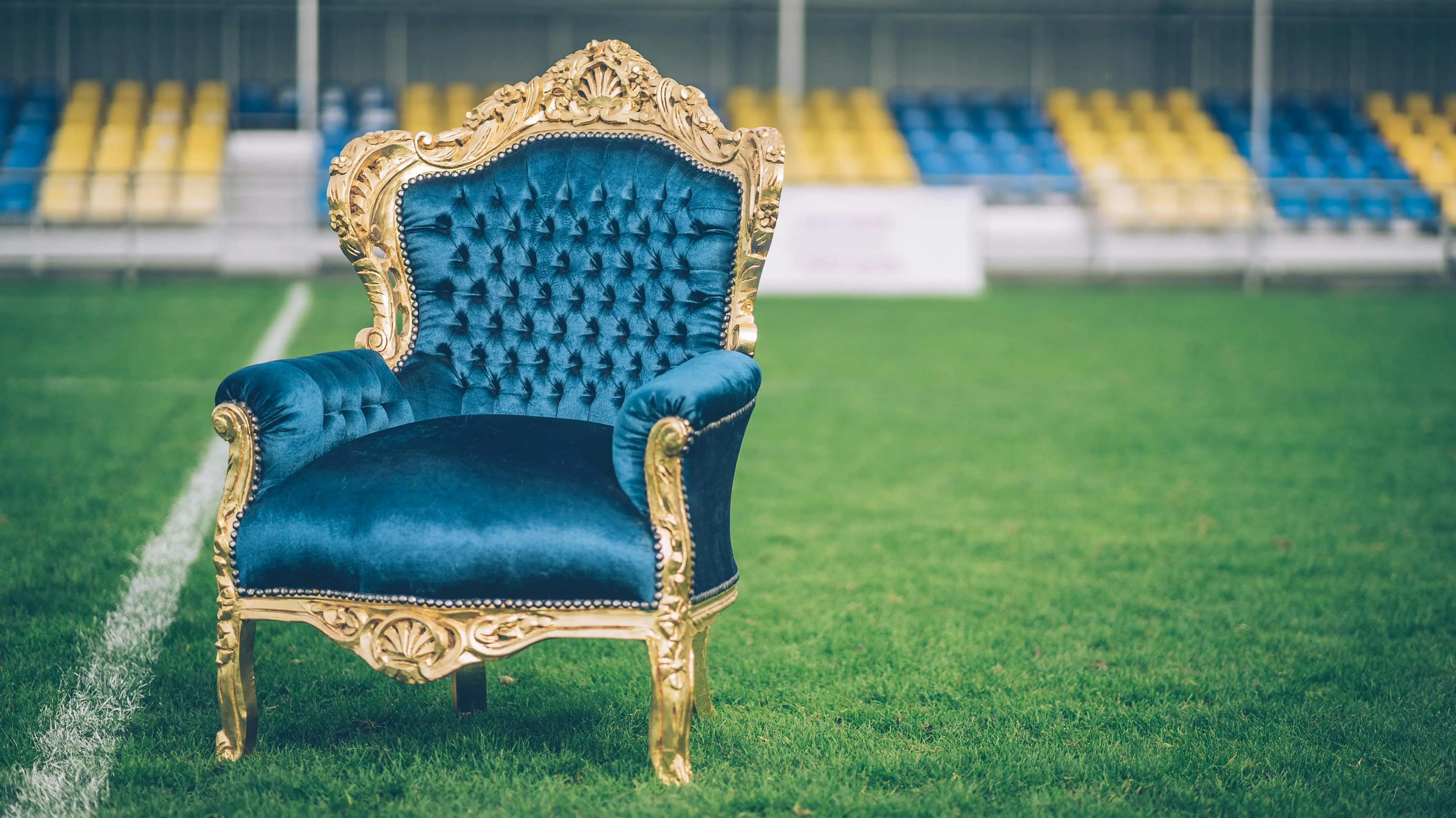 what might be placed in a secondary furniture A luxurious blue velvet and gold armchair sits prominently on a sports field.
