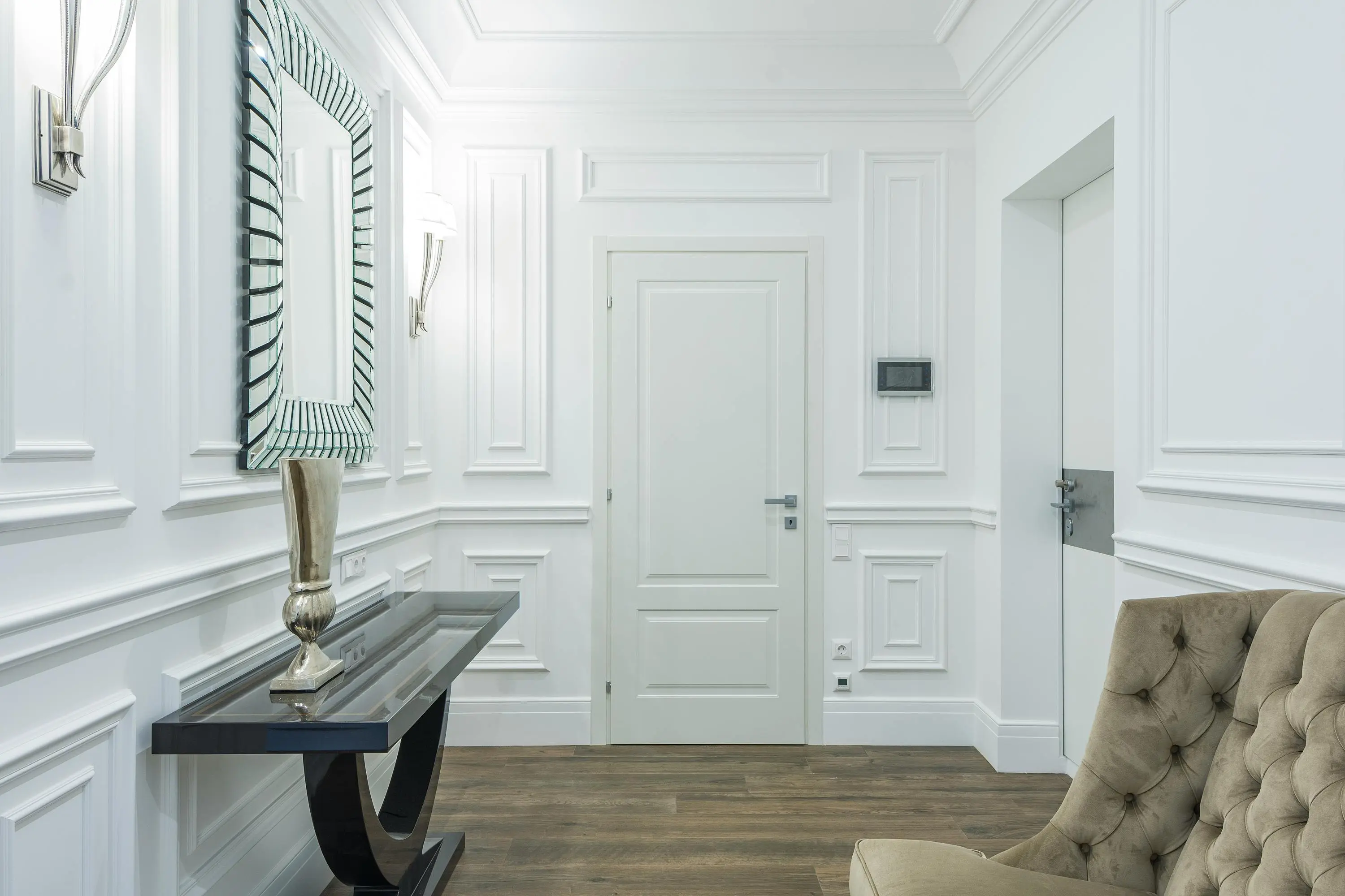 wall sculpture Sophisticated white interior with classic moldings and minimalist design, featuring a stylish mirrored wall and cozy seating.