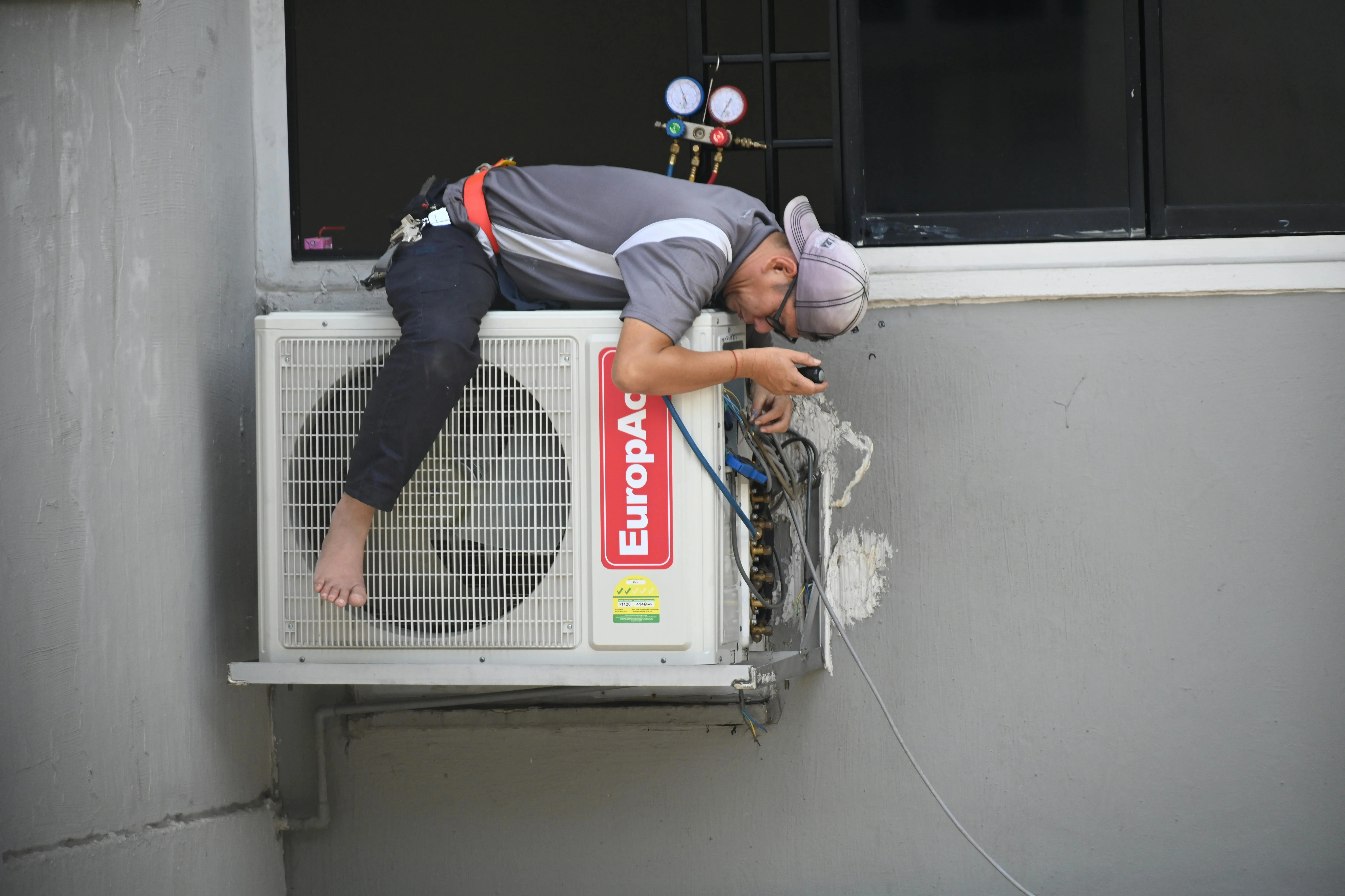 ac stopped working A technician skillfully repairing an outdoor air conditioning unit mounted on a building wall.