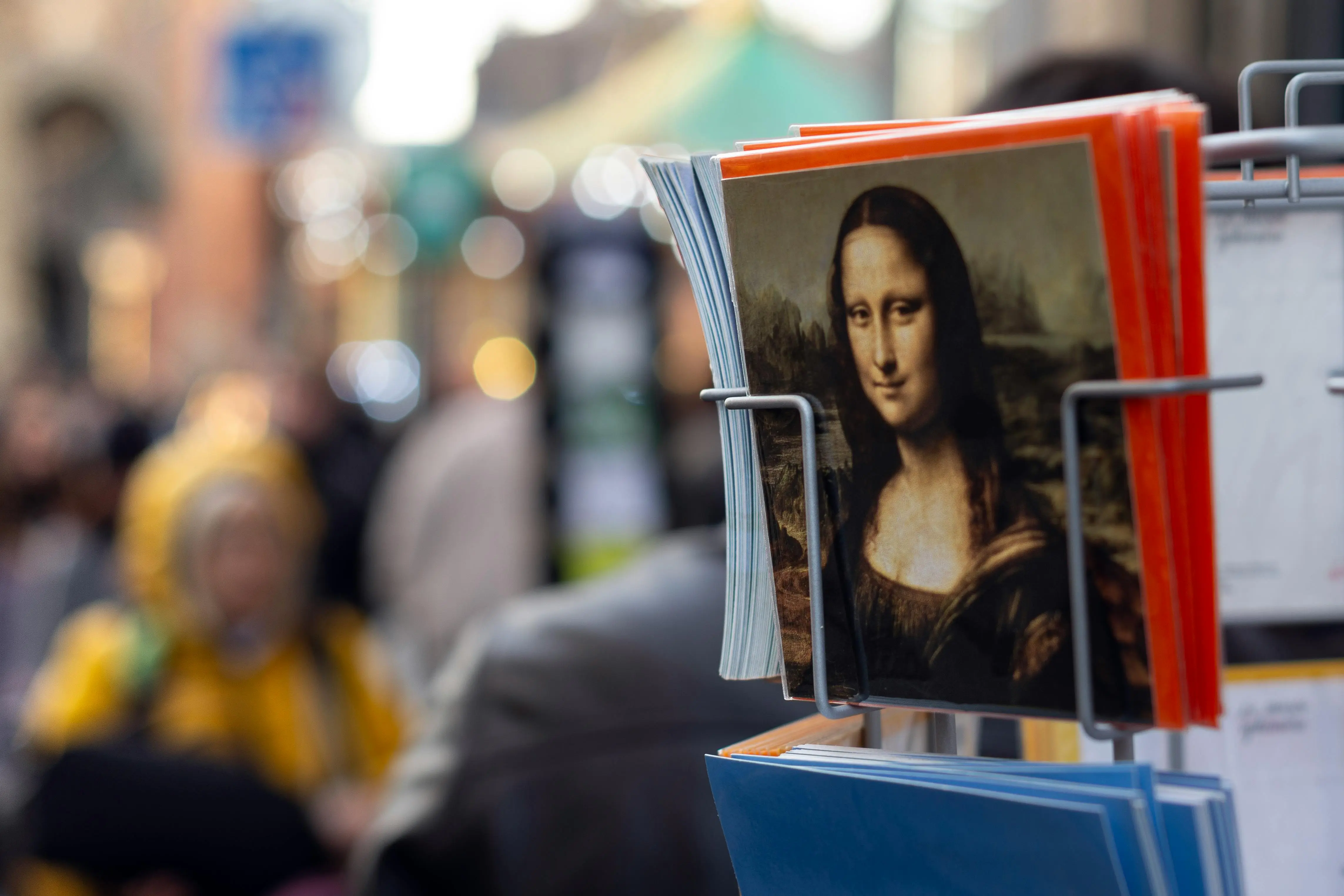 famous and easy paintings Street display of Mona Lisa postcards in Paris, featuring blurred background of pedestrians.