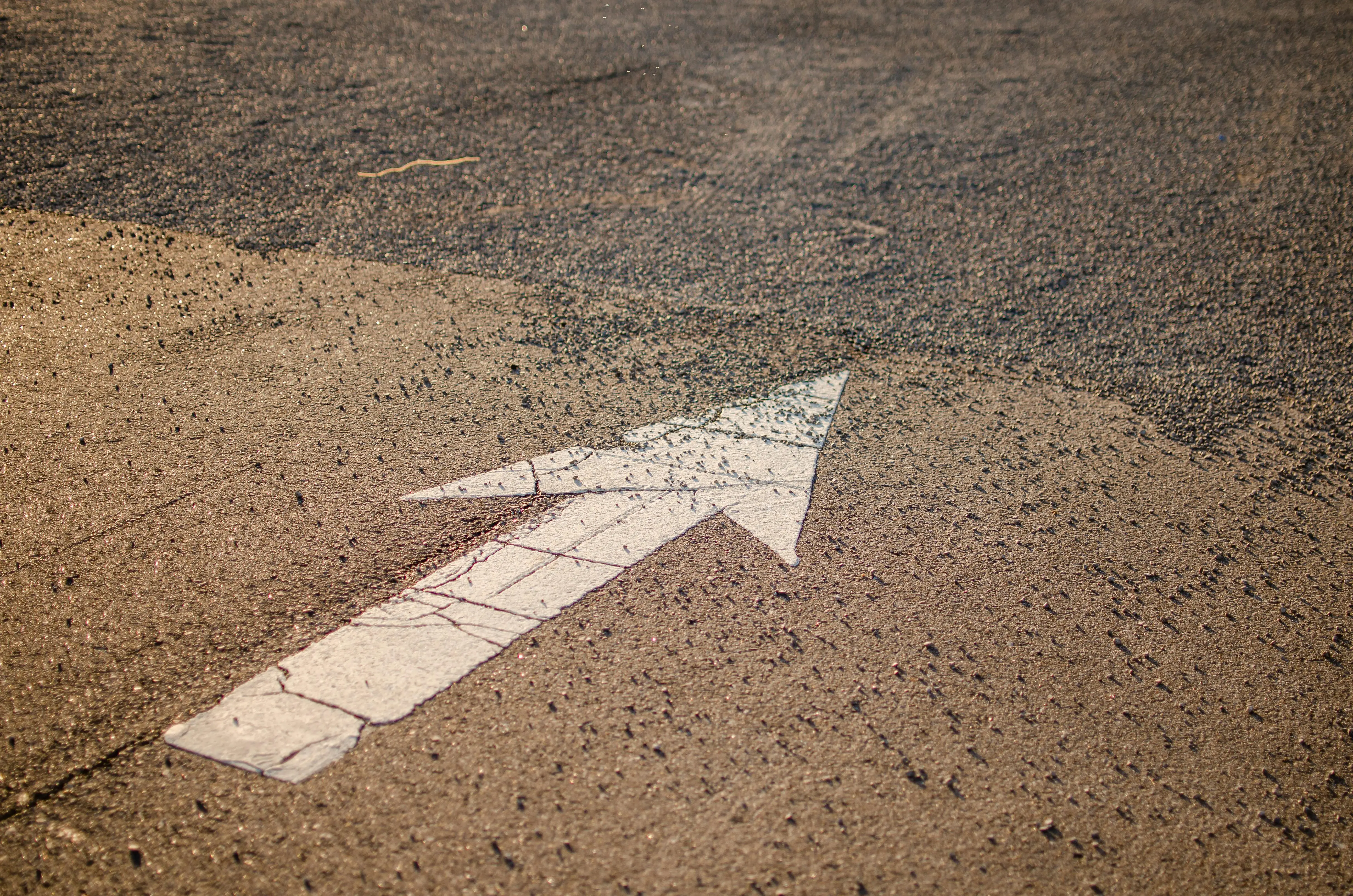 laundry signs A white directional arrow on a textured asphalt road surface under bright sunlight.