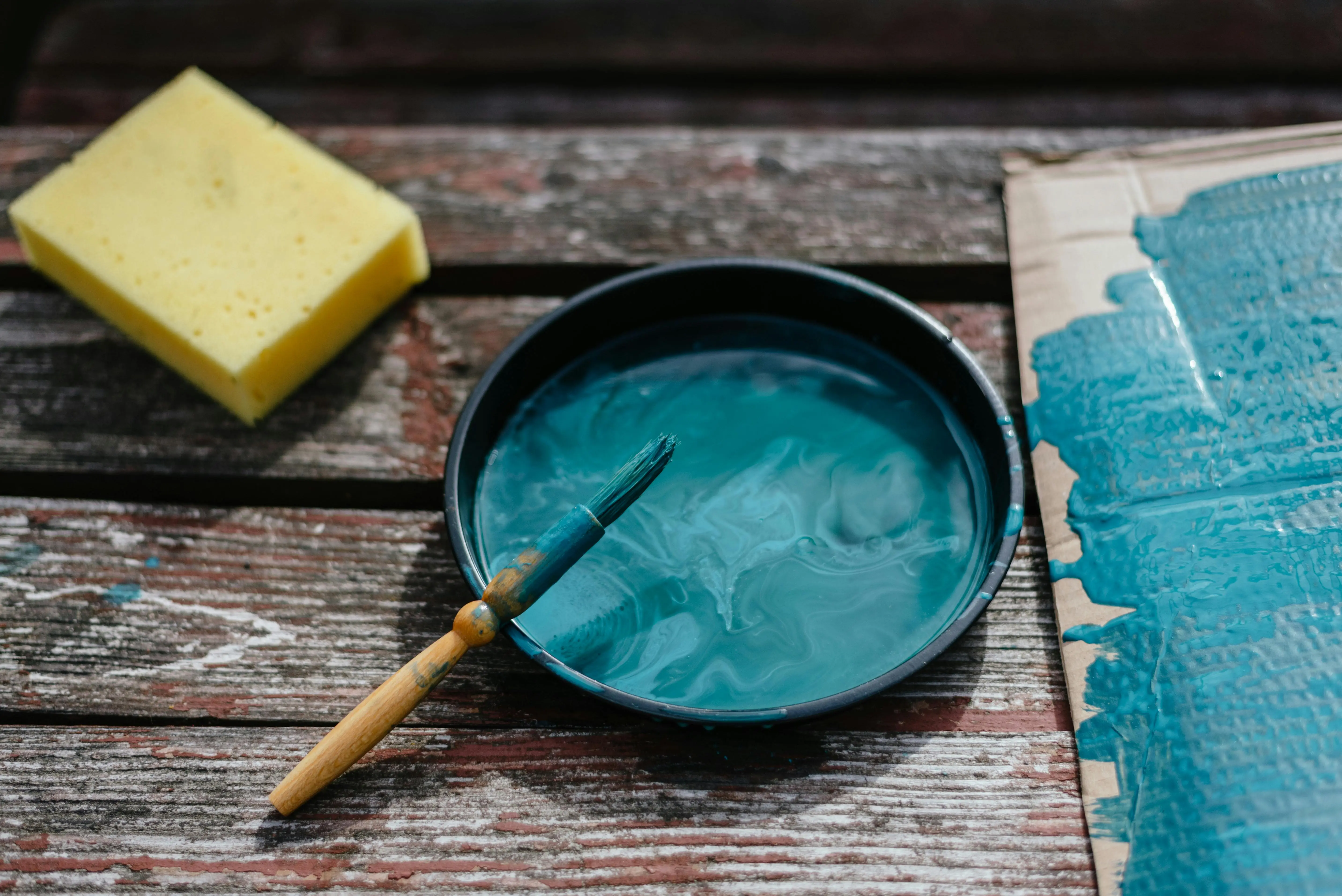 painted furniture chalk paint From above of turquoise paint in bowl with brush placed on wooden board near cardboard and sponge during repair work