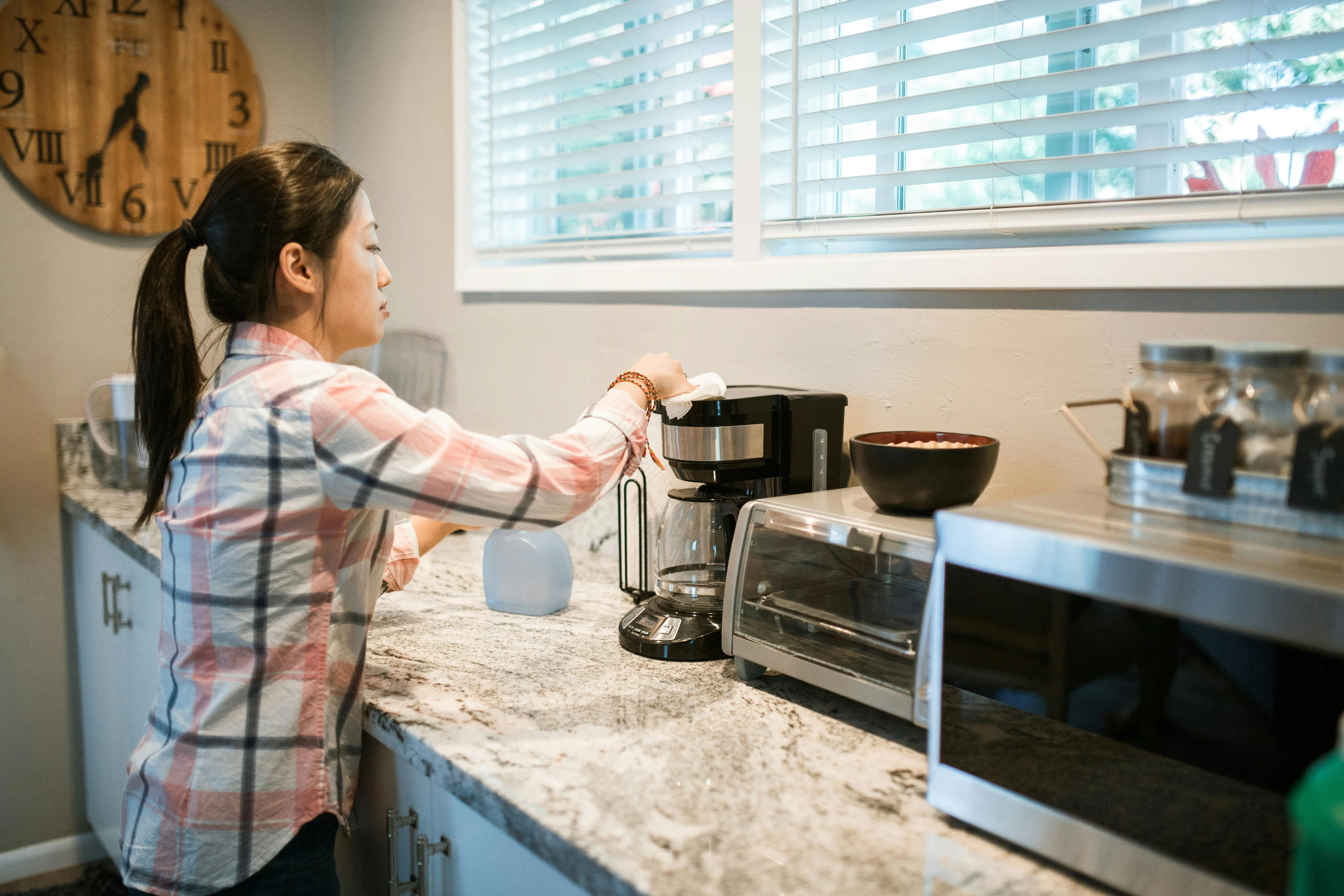 white granite colors Woman cleaning a coffee maker in a bright, modern kitchen with appliances.