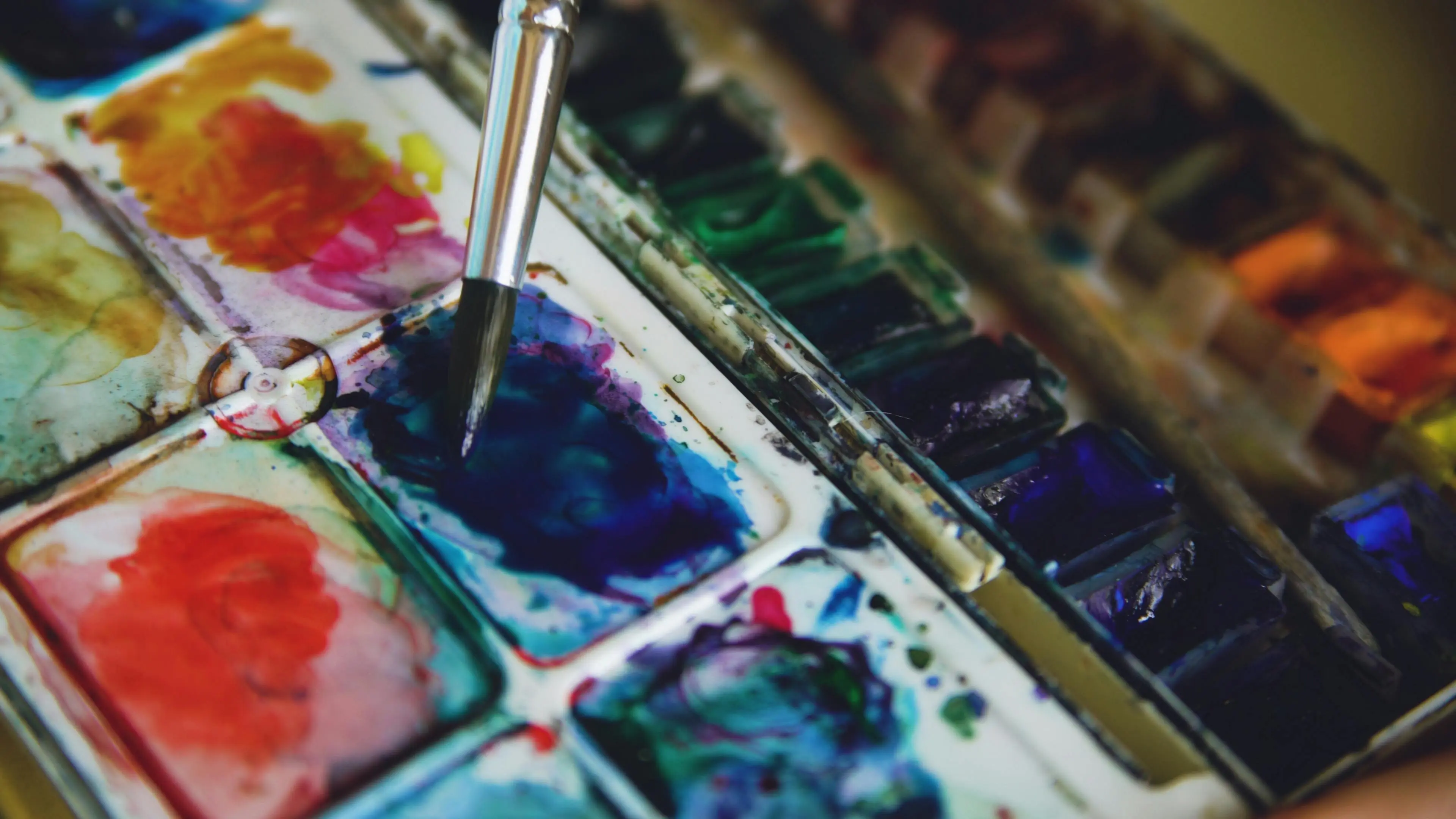 watercolor paint set Close-up of a watercolor palette with vibrant paints and a paintbrush in action.