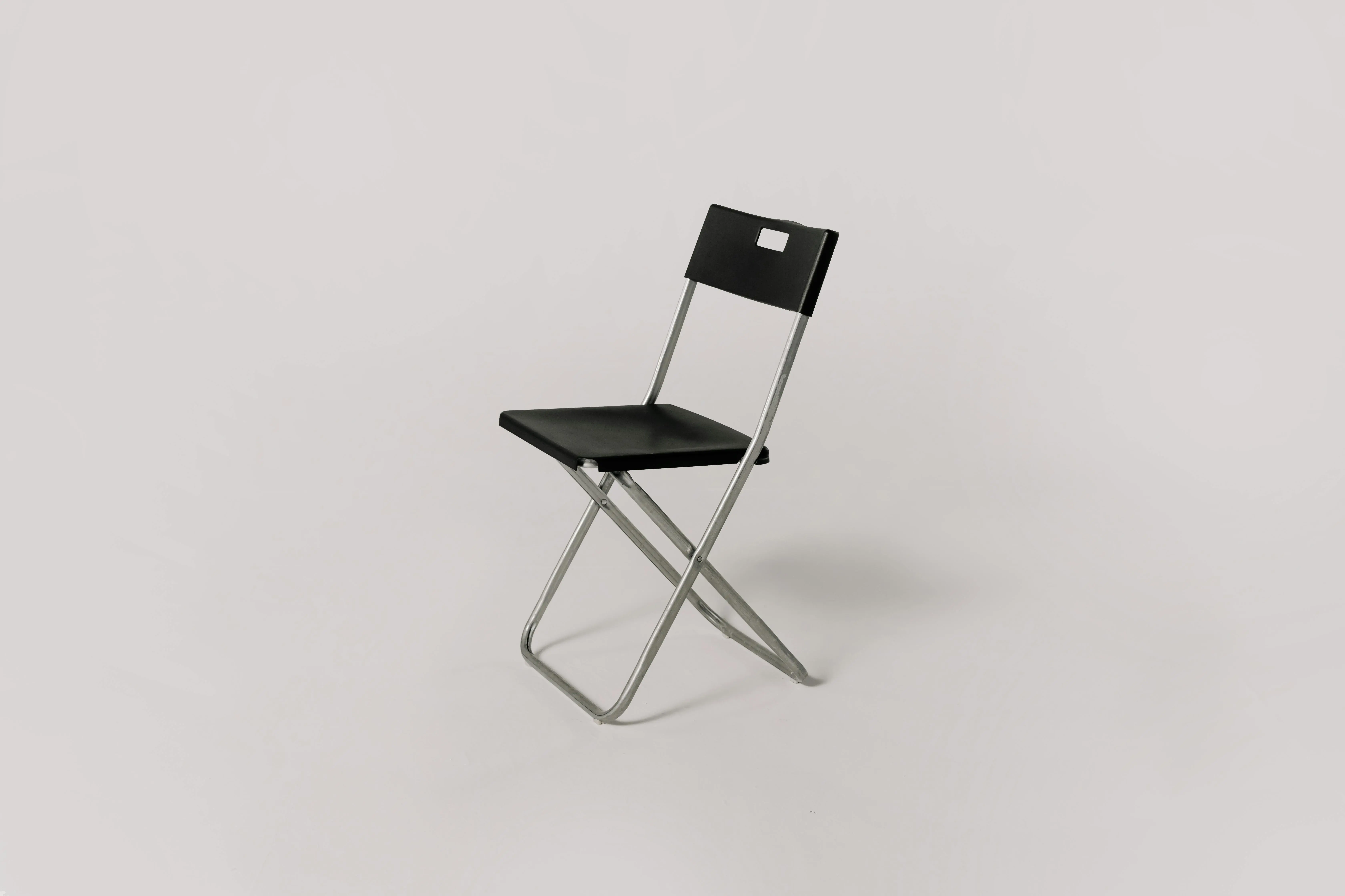 living in a tiny home tips Minimalistic photo of a black folding chair against a plain gray background, ideal for studio shoot representation.
