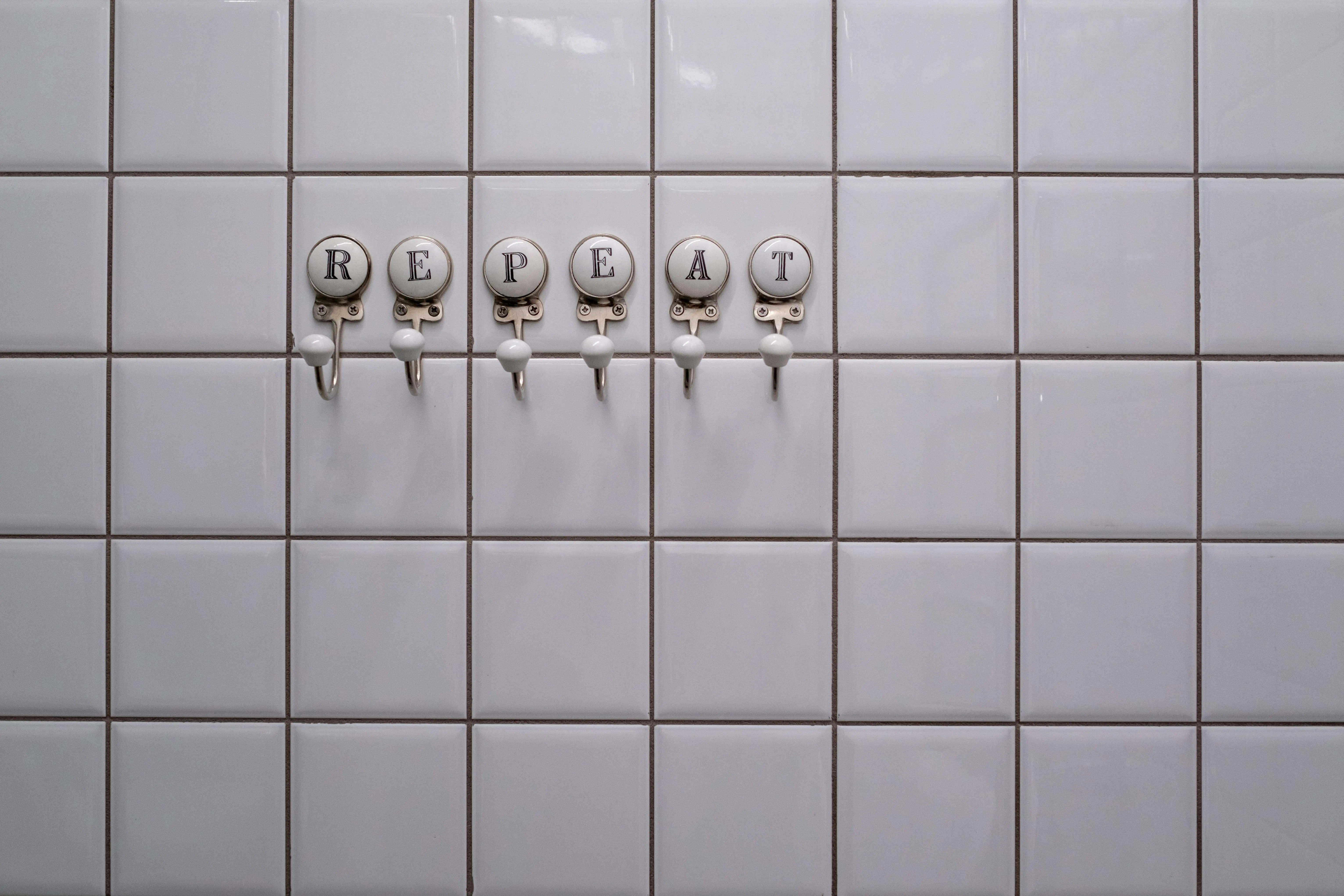white tiles White tiled wall with towel hooks spelling 'REPEAT', showcasing a conceptual minimalist design.