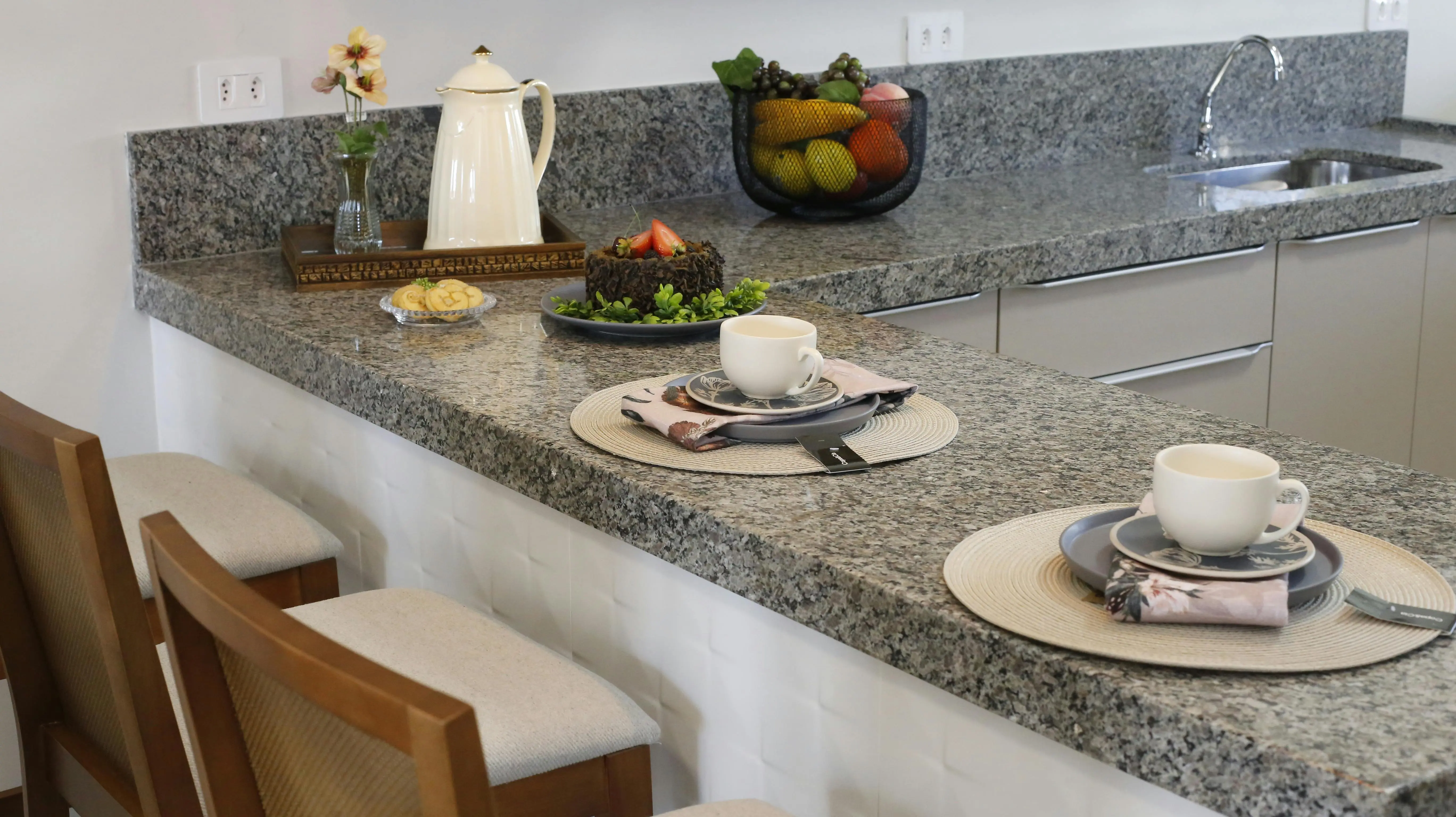 white granite colors A cozy kitchen counter setup with two places set for breakfast, featuring cups and a cake.