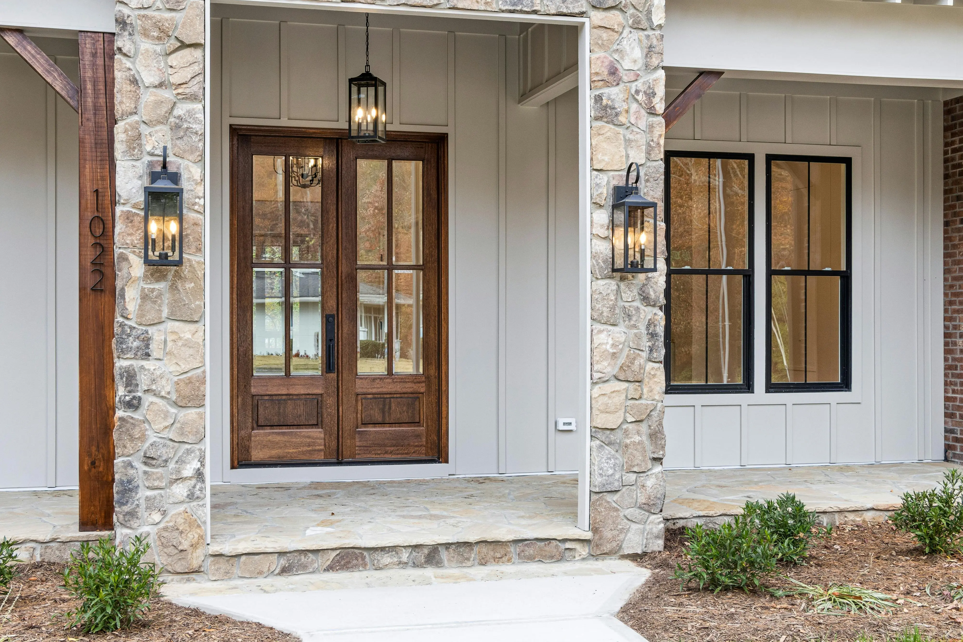 exterior wall lantern A contemporary stone facade with wooden double doors and lantern-style lighting.