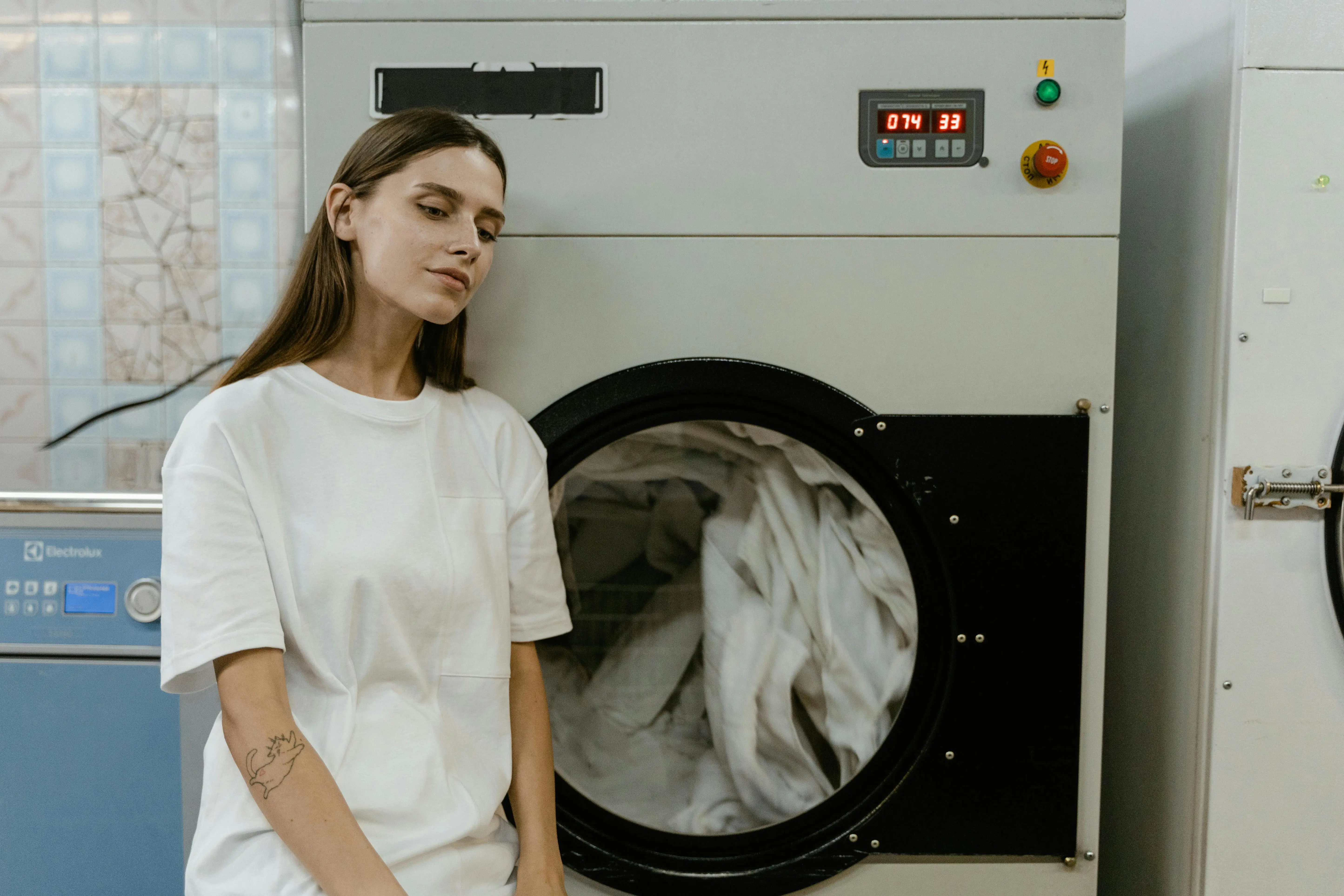 laundry signs A woman in a laundry facility standing by a washing machine, contemplating the process.