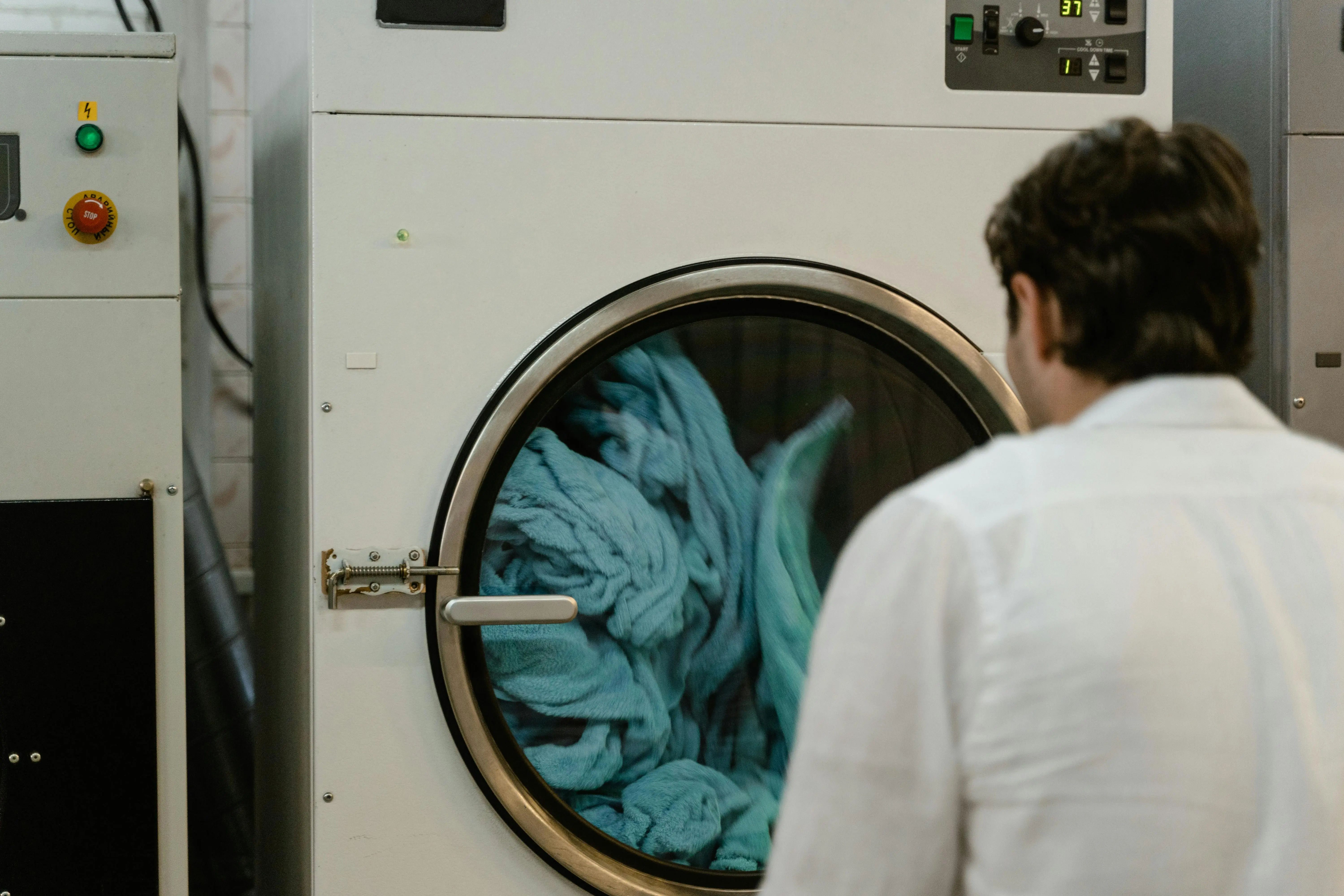 get blood out of clothes A man watches a washing machine spin in a laundromat, focusing on the process.