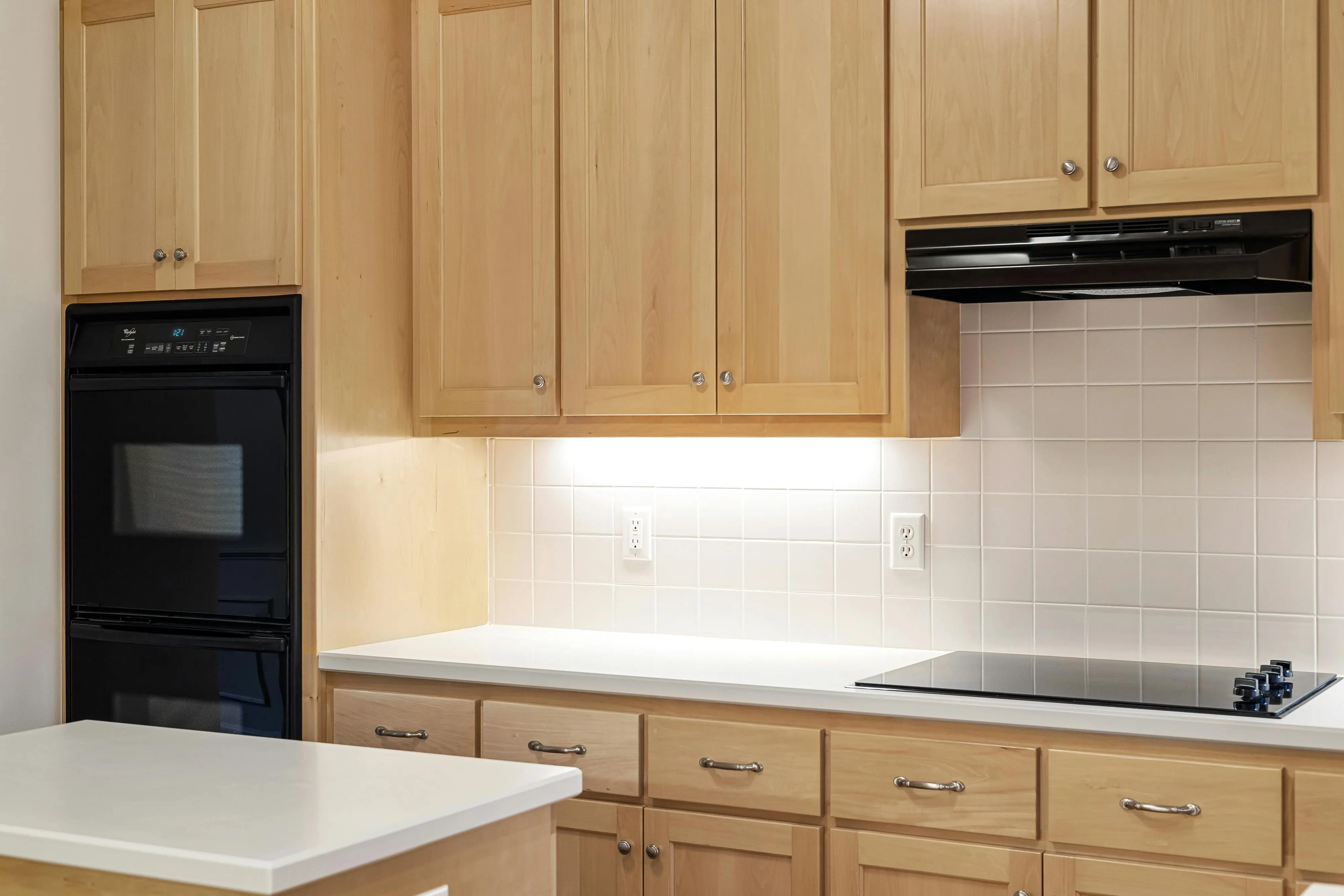 maple cabinets Sleek kitchen featuring wooden cabinets, black oven, and induction stove.