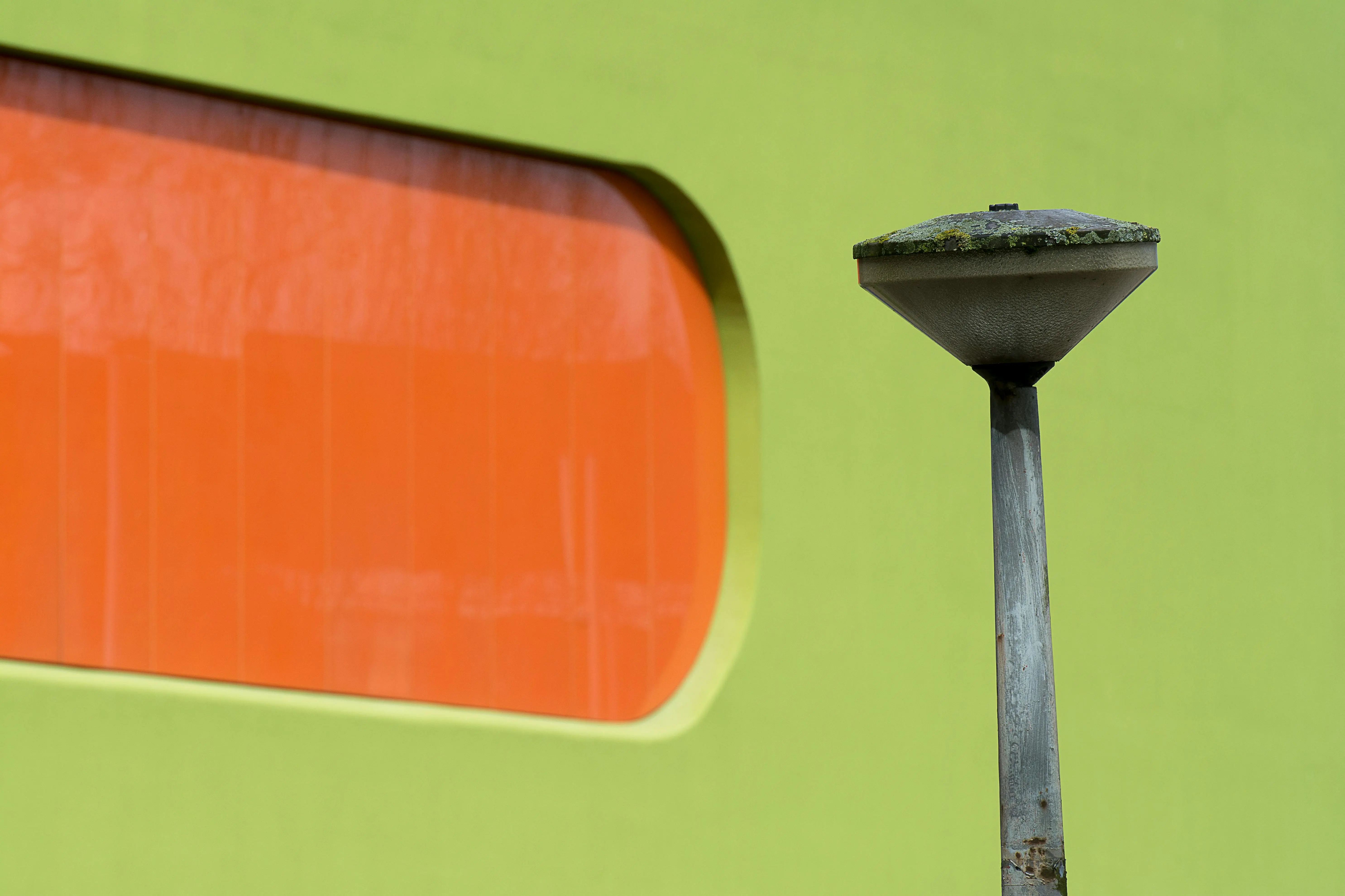 mid century modern art A striking green wall features an orange window, complemented by a weathered streetlamp.