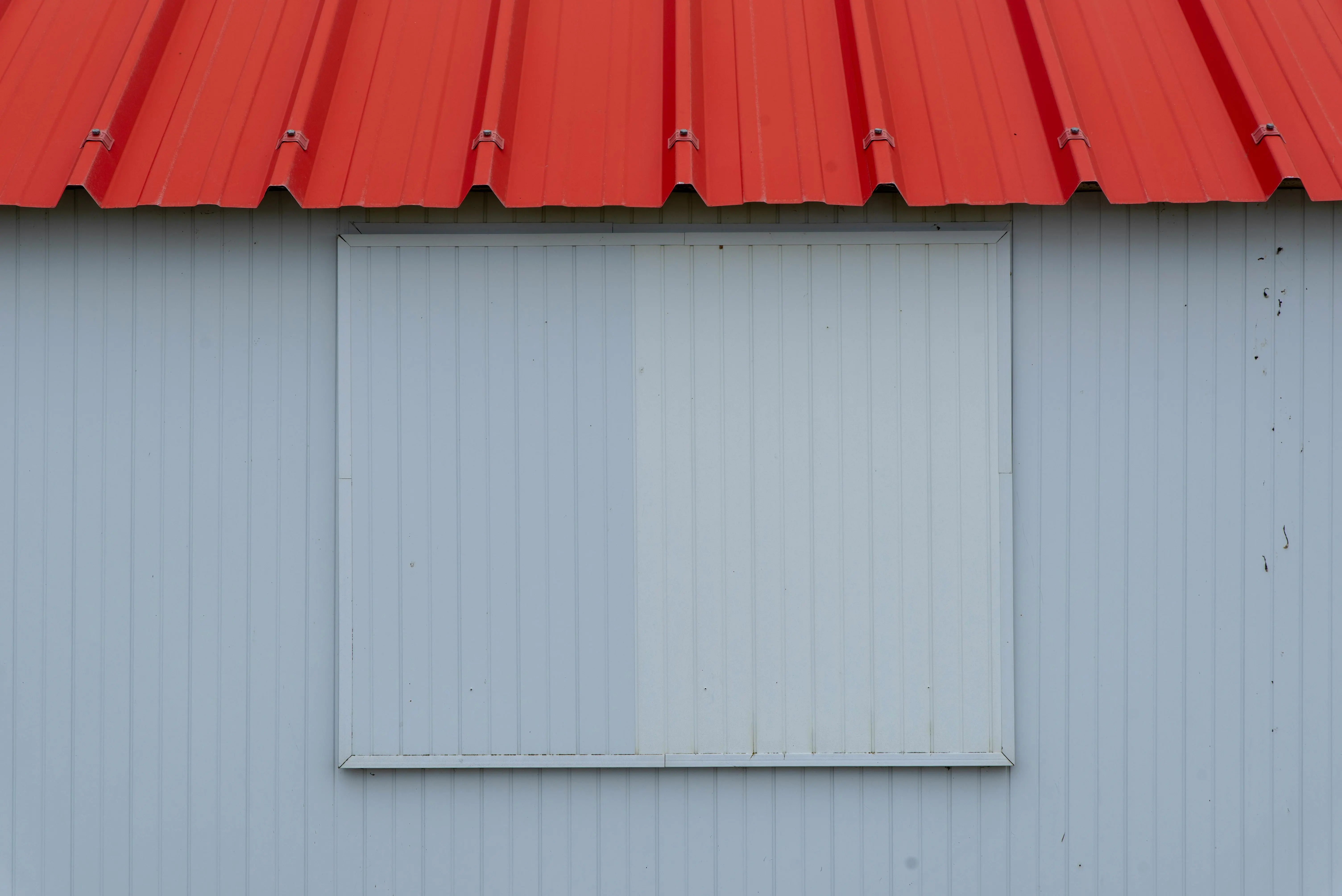 metal roof sealant Minimalist image of a red metal roof with blue-grey corrugated panel wall.