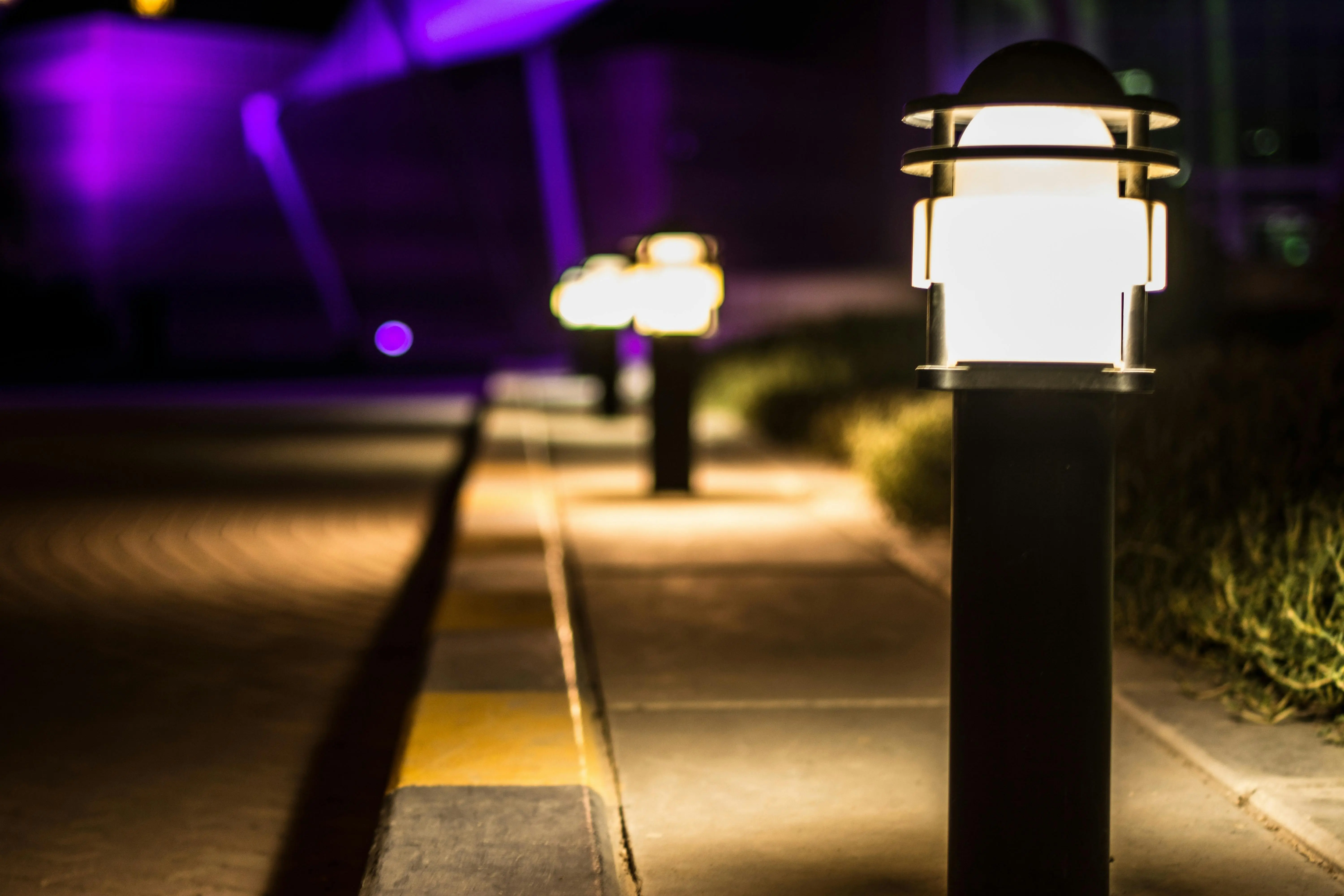 pathway lights A scenic night view of illuminated lamp posts lining a paved path with a bokeh effect.